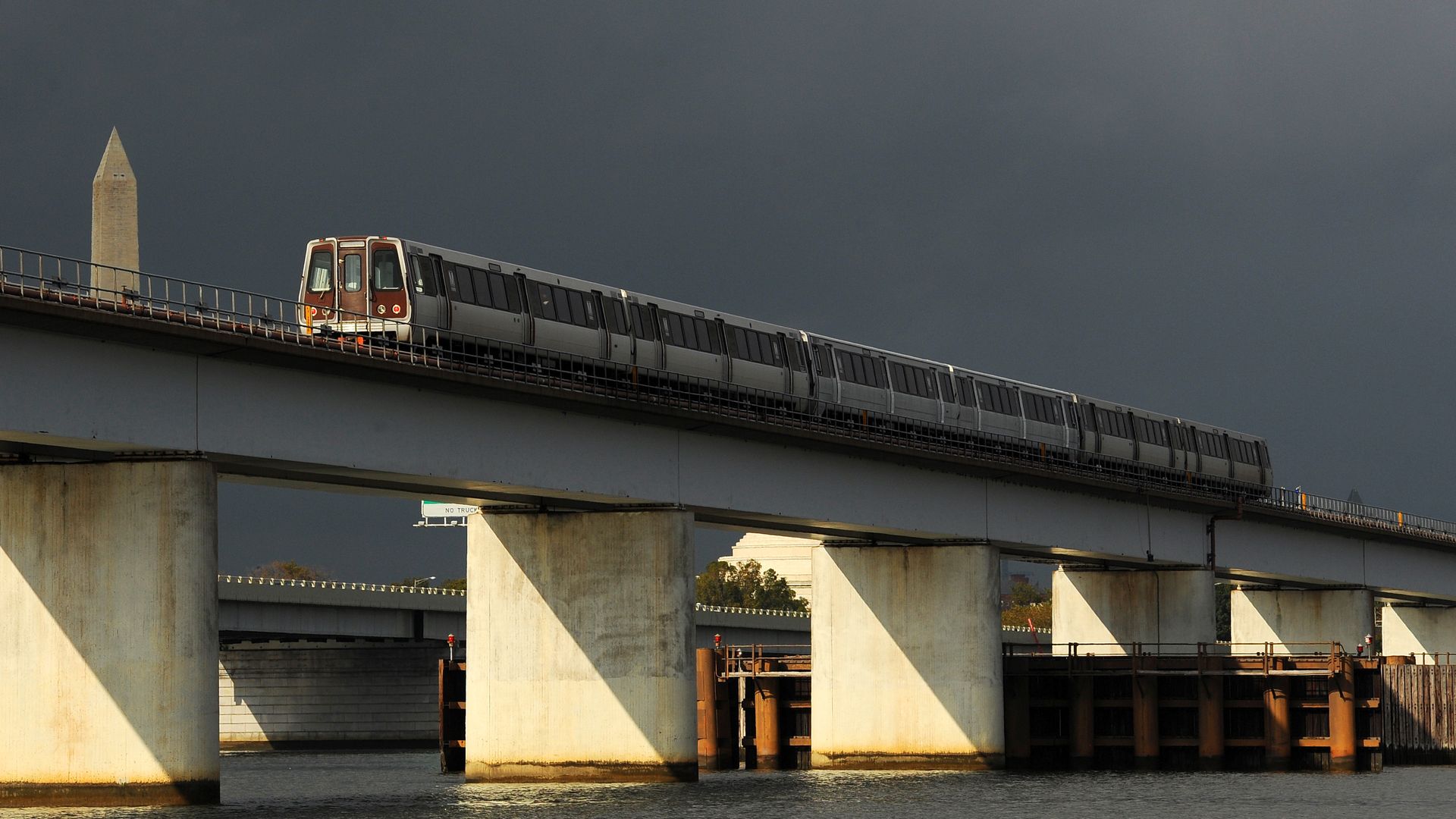 A Yellow Line train crosses a bridge over the Potomac River with the National Monument in the background.