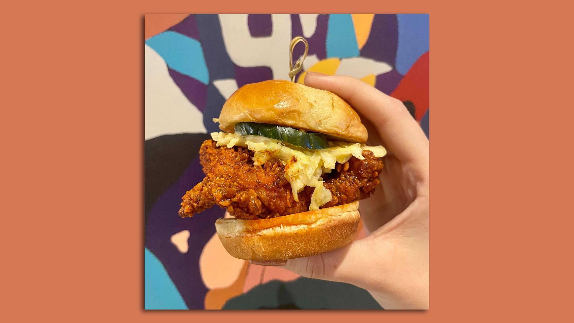 photo of chicken sandwich in front of colorful mural