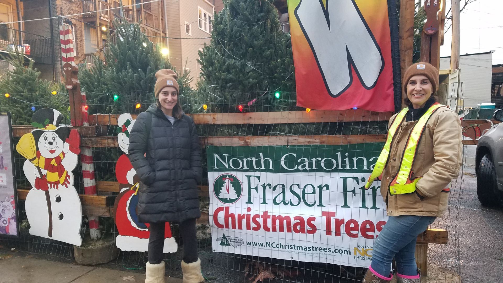 Photo of two women standing in front of a Christmas tree lot.