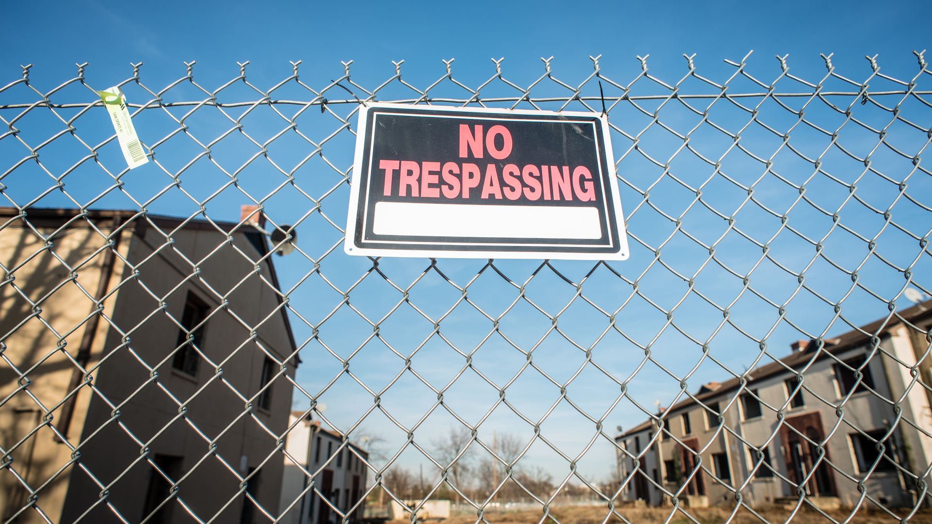 A "no trespassing" sign is on a fence with houses at Barry Farm in the background