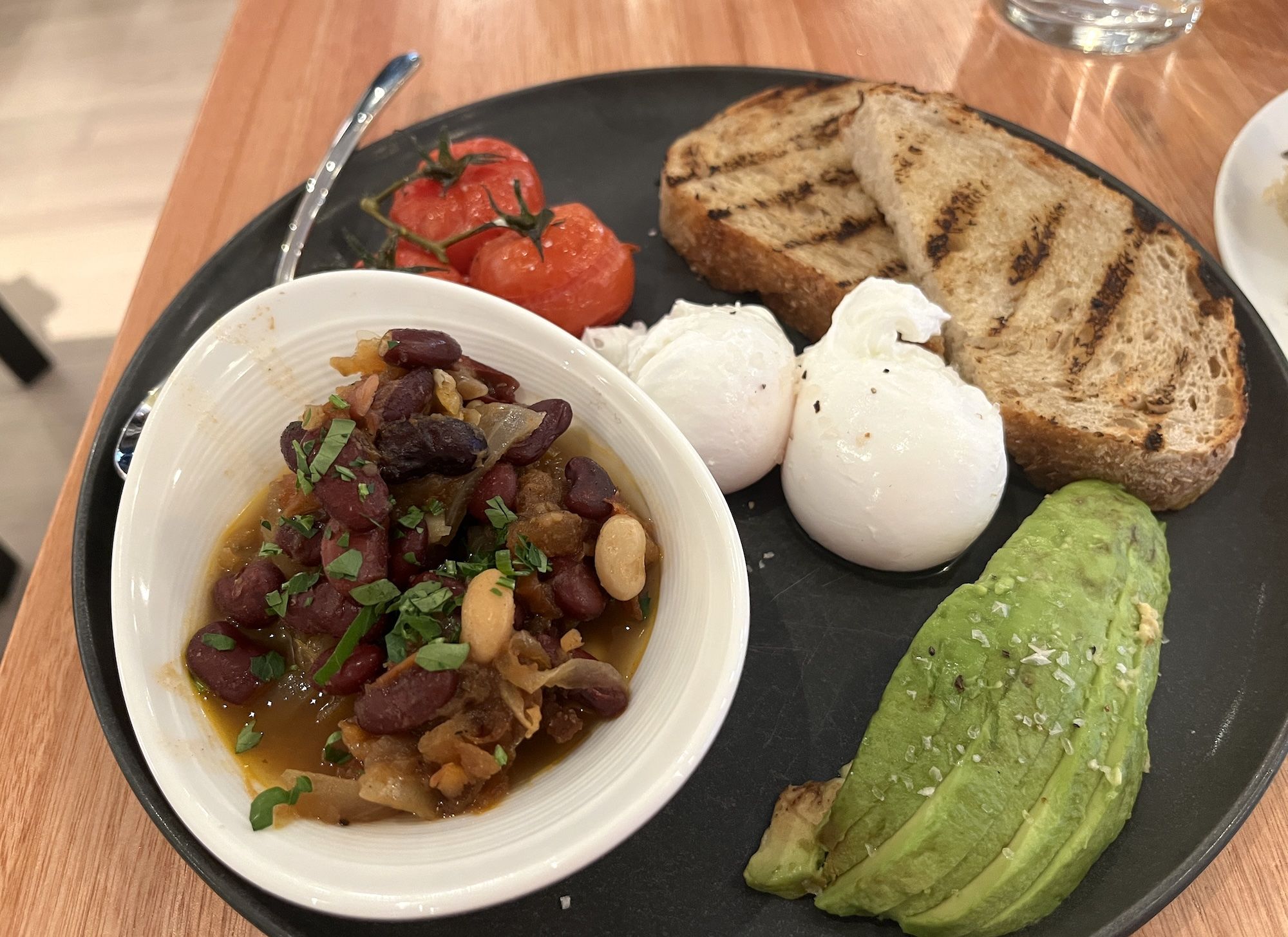 Dish with baked beans on a plate with poached eggs, roasted tomatoes, sliced avocado and toast.
