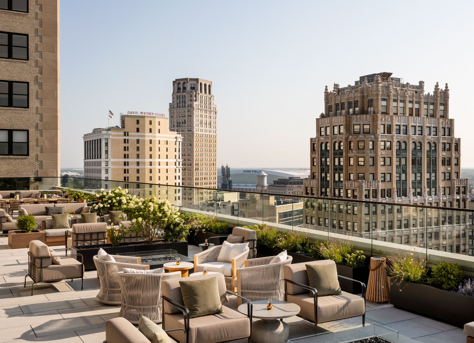 Rooftop terrace with outdoor sofas, chairs and potted plants, overlooking a Detroit's skyline