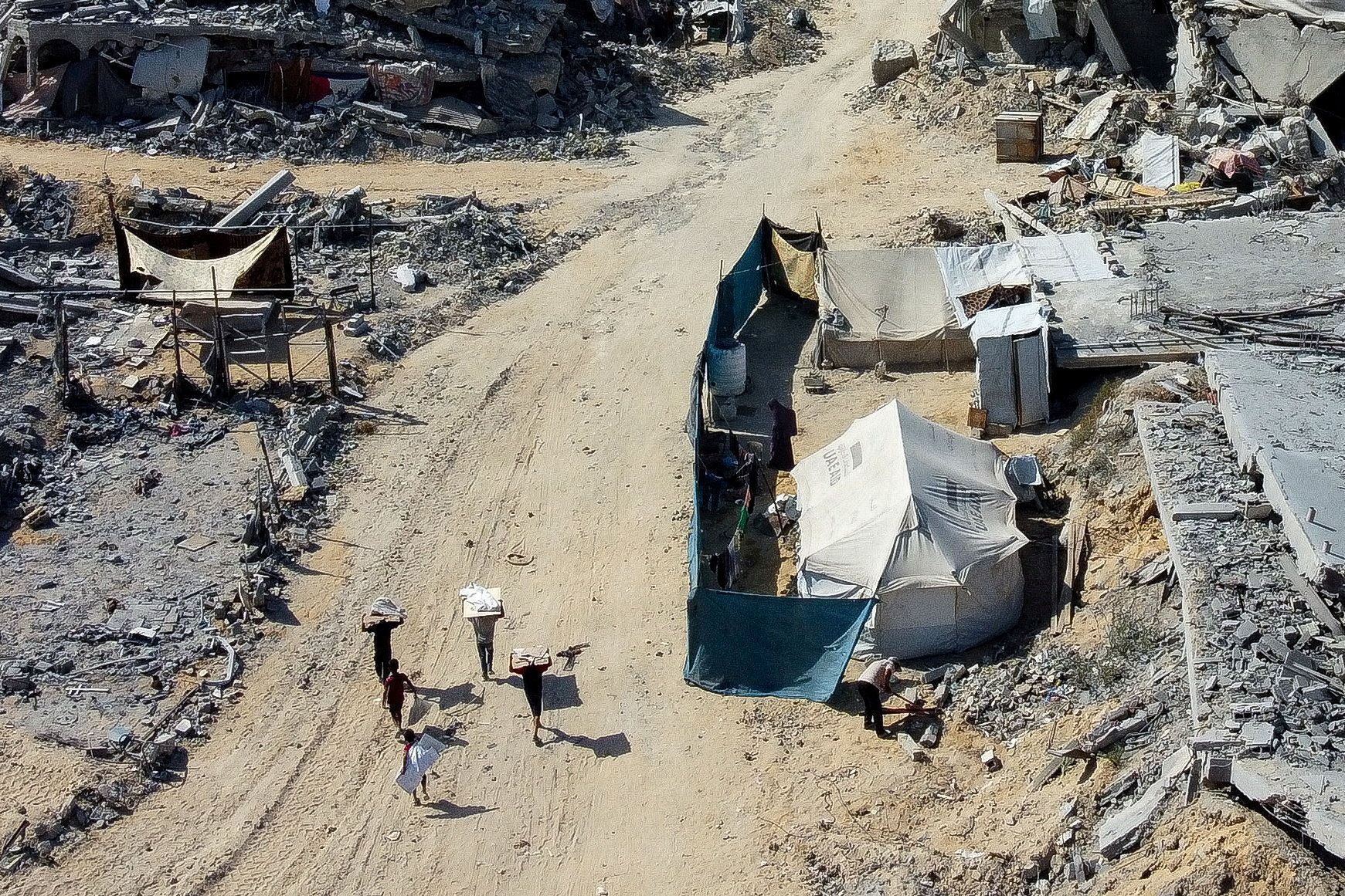 Aerial view of Palestinians walking among rubble and tents