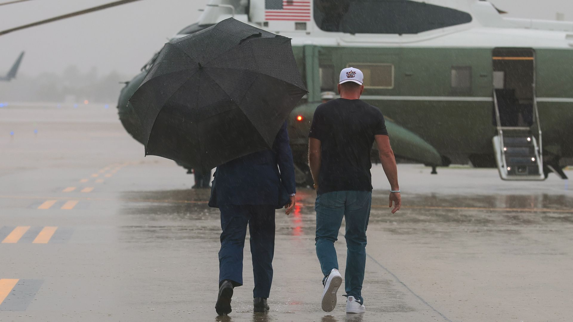 President Donald Trump carries an umbrella and walks alongside Pat McAfee to a helicopter. 