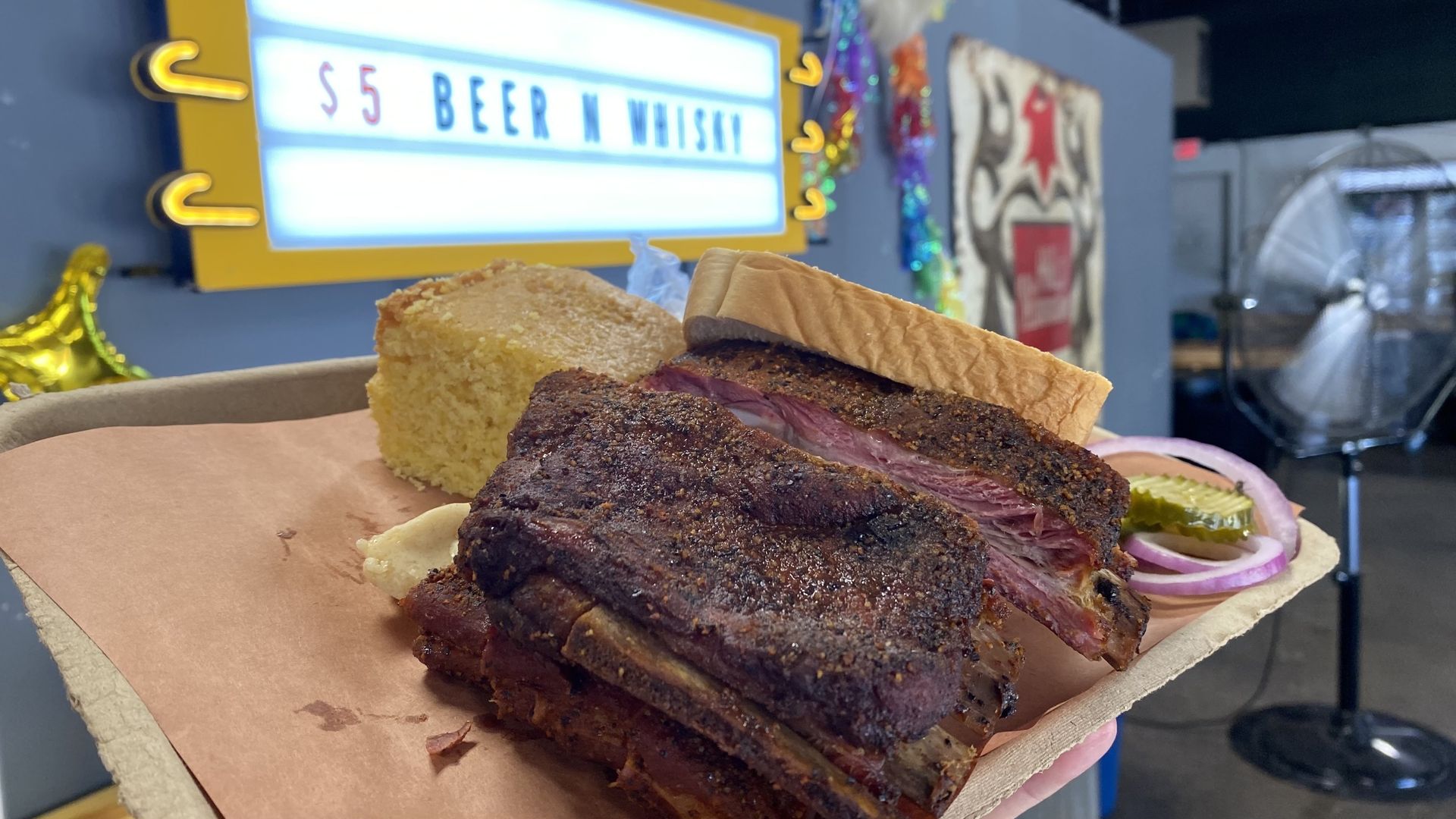 Photo of a plate with BBQ ribs and bread in front of a sign that reads: $5 beer and whiskey