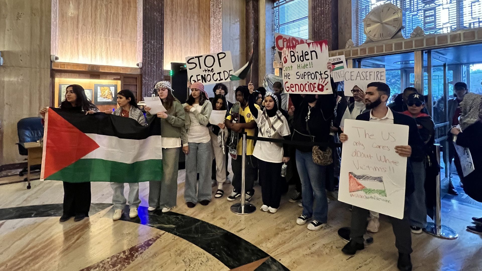 Photo of people holding a Palestine flag and posters in a lobby.