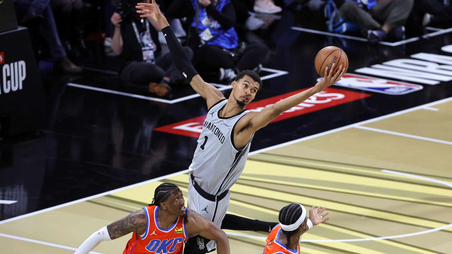 The Spurs' Victor Wembanyama pulls in a pass over Jalen Williams and Shai Gilgeous-Alexander of the Oklahoma City Thunder on Saturday in the fourth quarter. Wembanyama is seen towering above the two. The Spurs' victory sent them to the NBA Cup Finals on Tuesday.