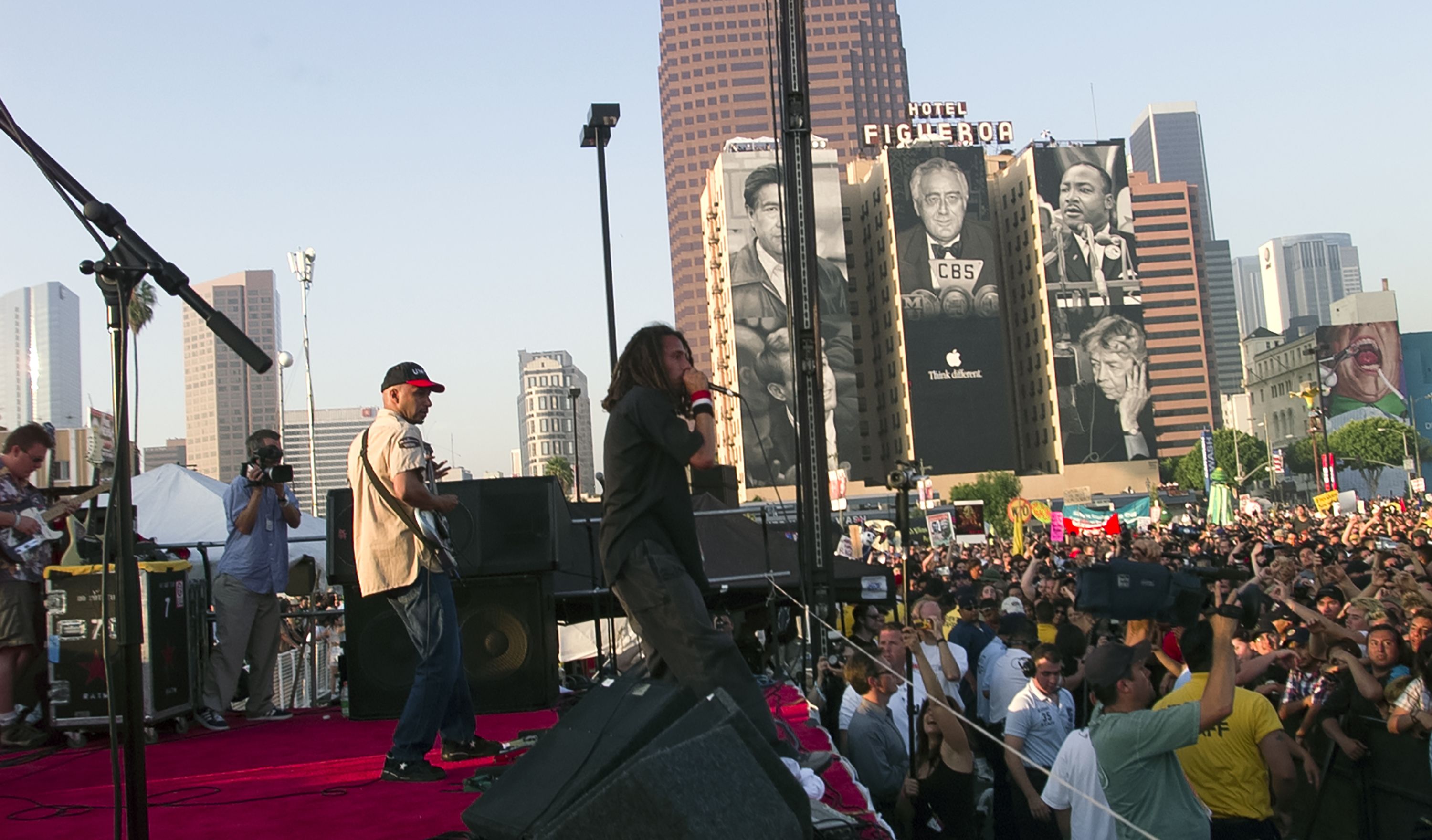 Photo of musicians playing music on stage in front of a crowd of people outside. 