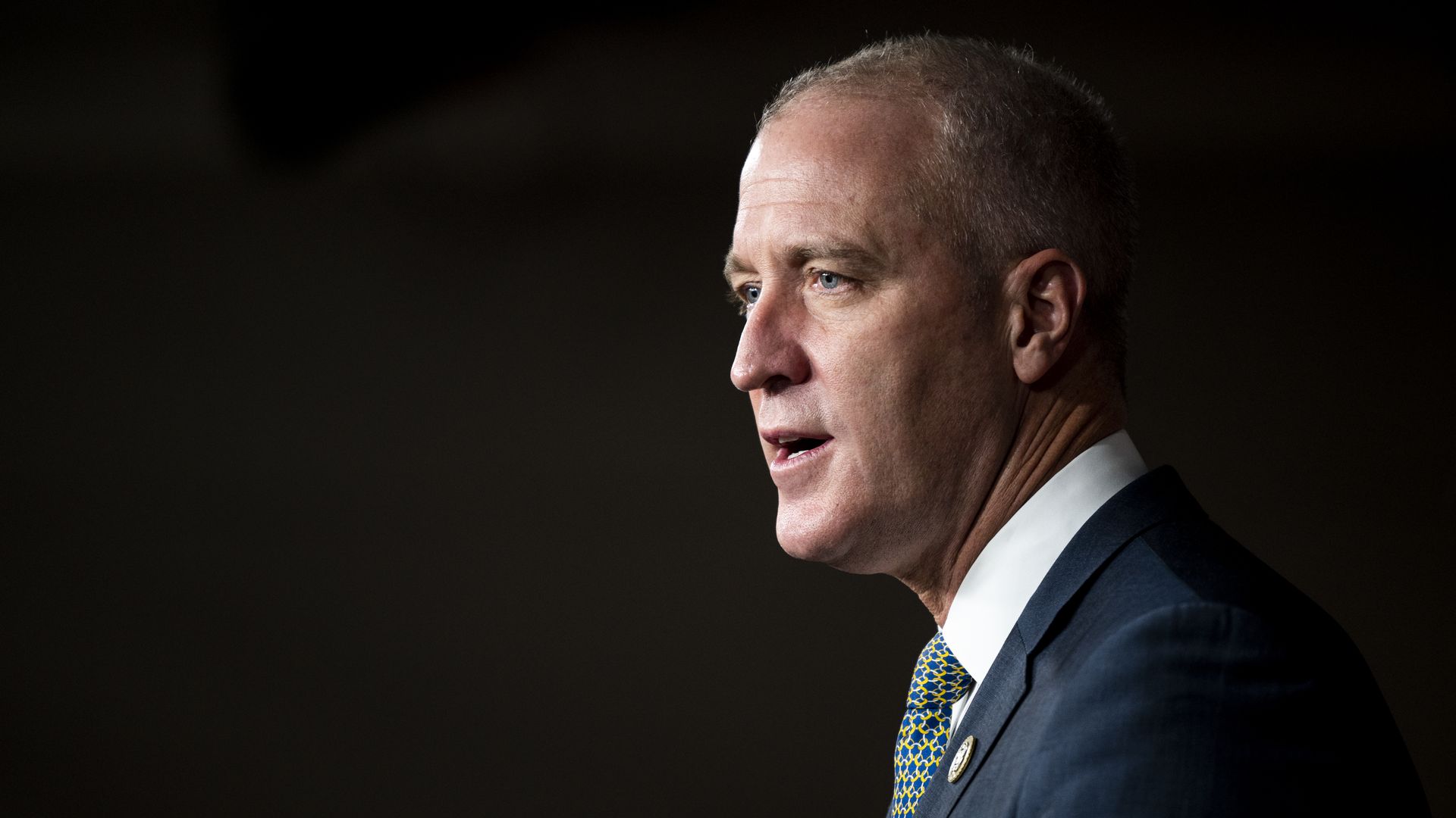 Rep. Sean Patrick Maloney wearing a blue suit jacket, yellow and blue tie and congressional pin against a black backdrop.