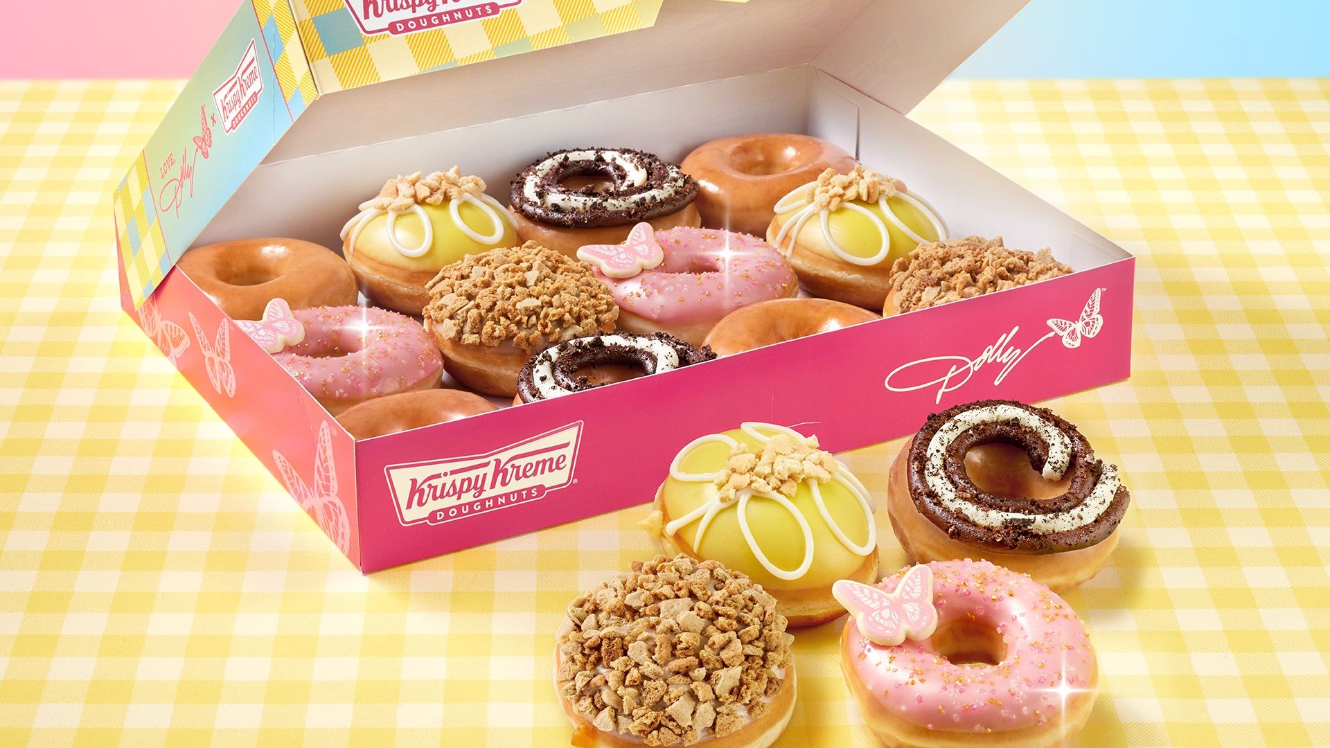 Box of Krispy Kreme doughnuts full of doughnuts with four doughnuts in front of box on yellow checkered tablecloth