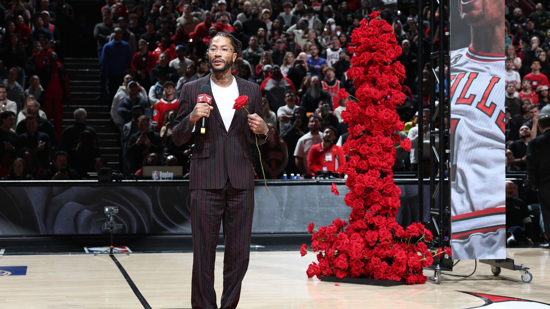 Photo of a man standing in front of a screen with a microphone talking to a crowd at a stadium
