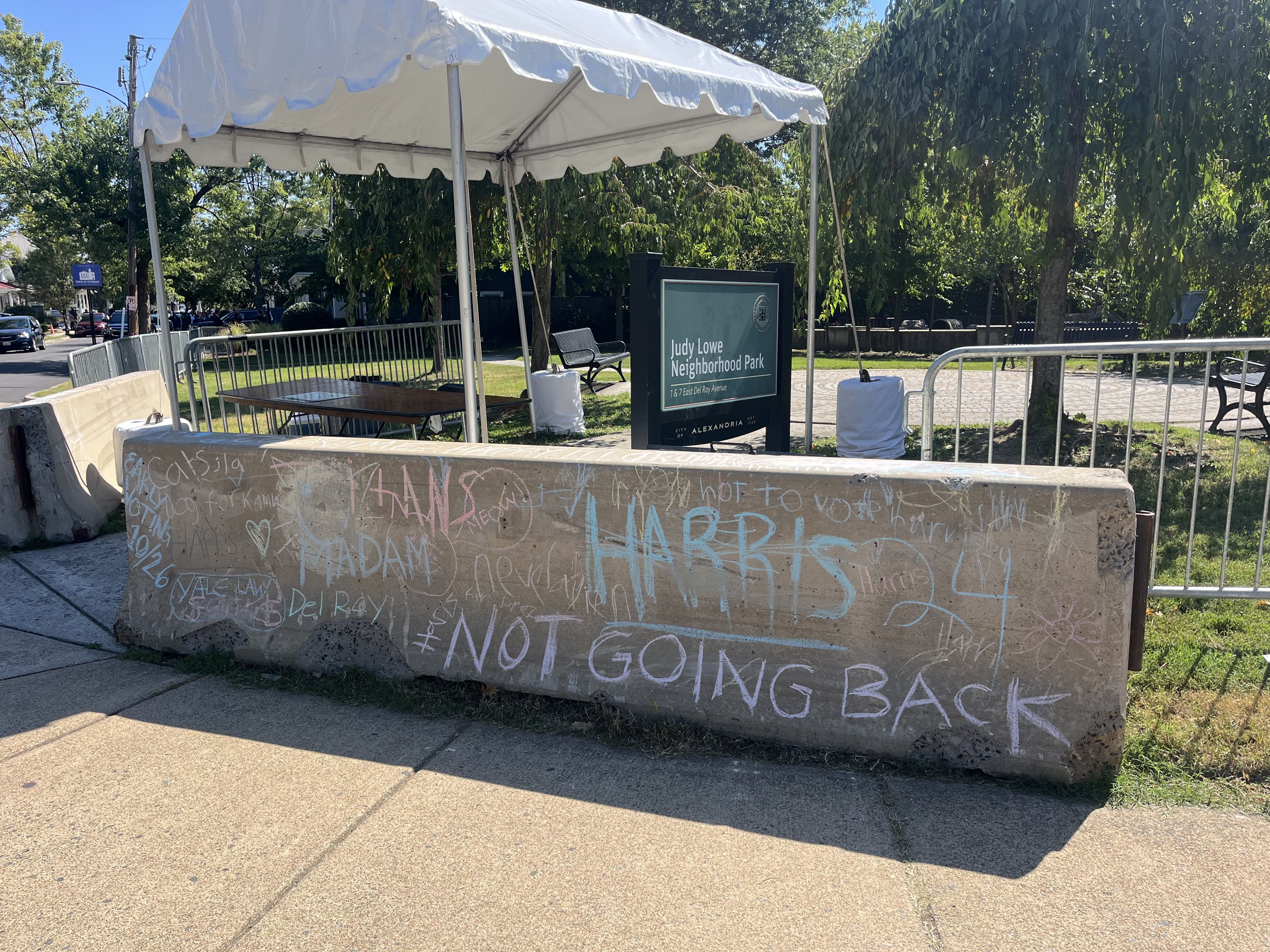 A photo showing a concrete barricade with chalk graffiti reading "Harris '24" and "Not Going Back."