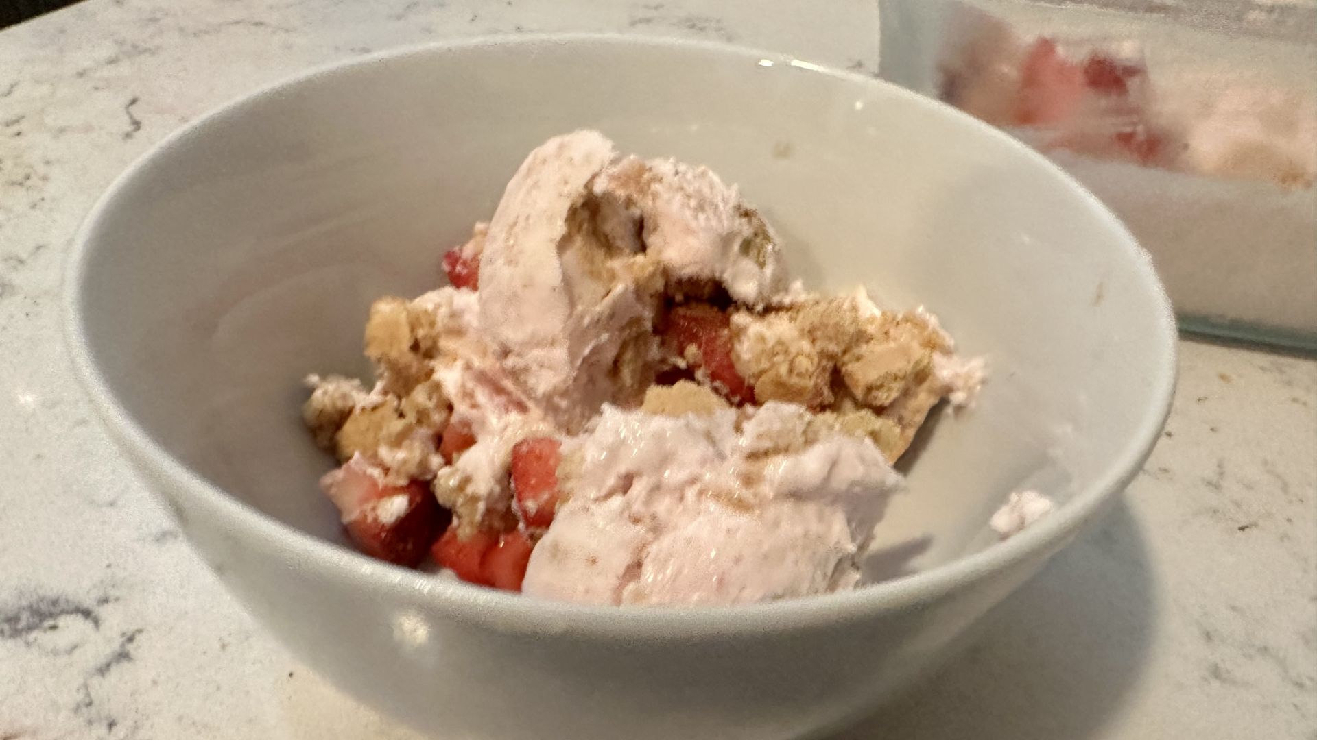Something looking vaguely like strawberry ice cream in a bowl with more strawberries and graham crackers.