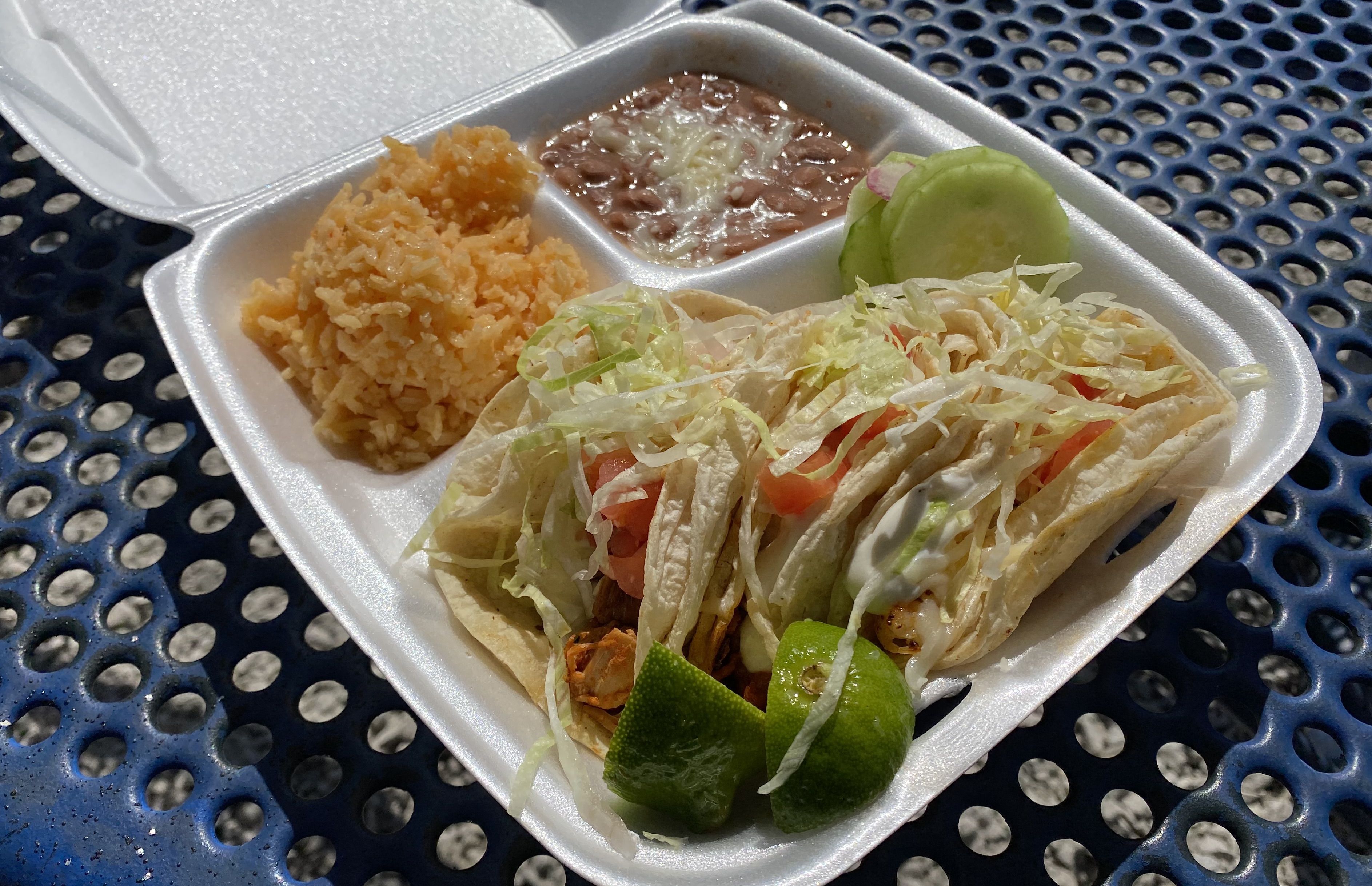 A sytrofoam container with three sections, with tacos, rice and beans