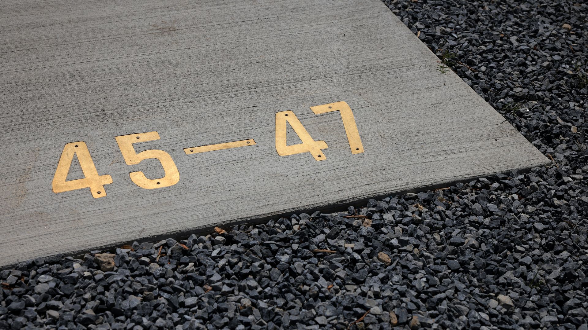 Metal numbers reading "45-47" are embedded in a concrete sidewalk near the White House ballroom construction site.