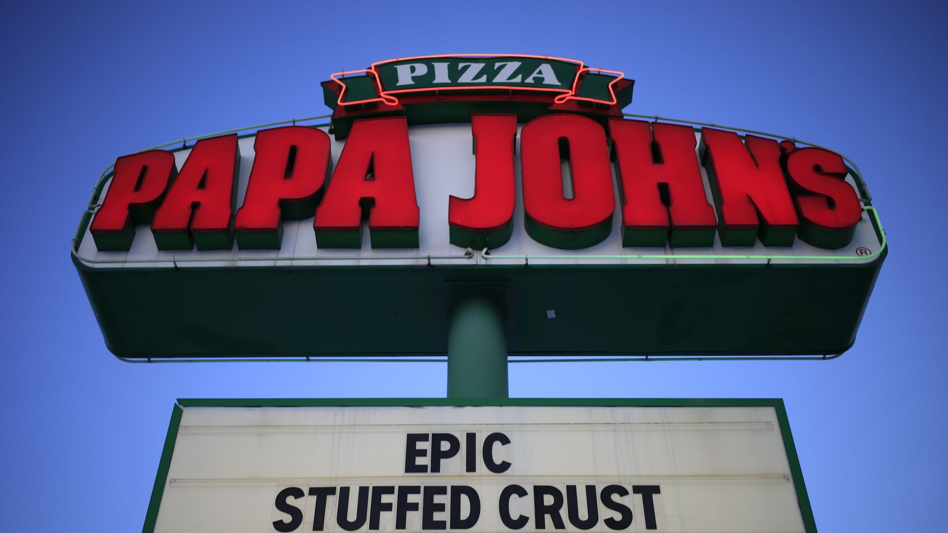 A Papa John's sign towers into the blue sky, its name spelled out in red letters.