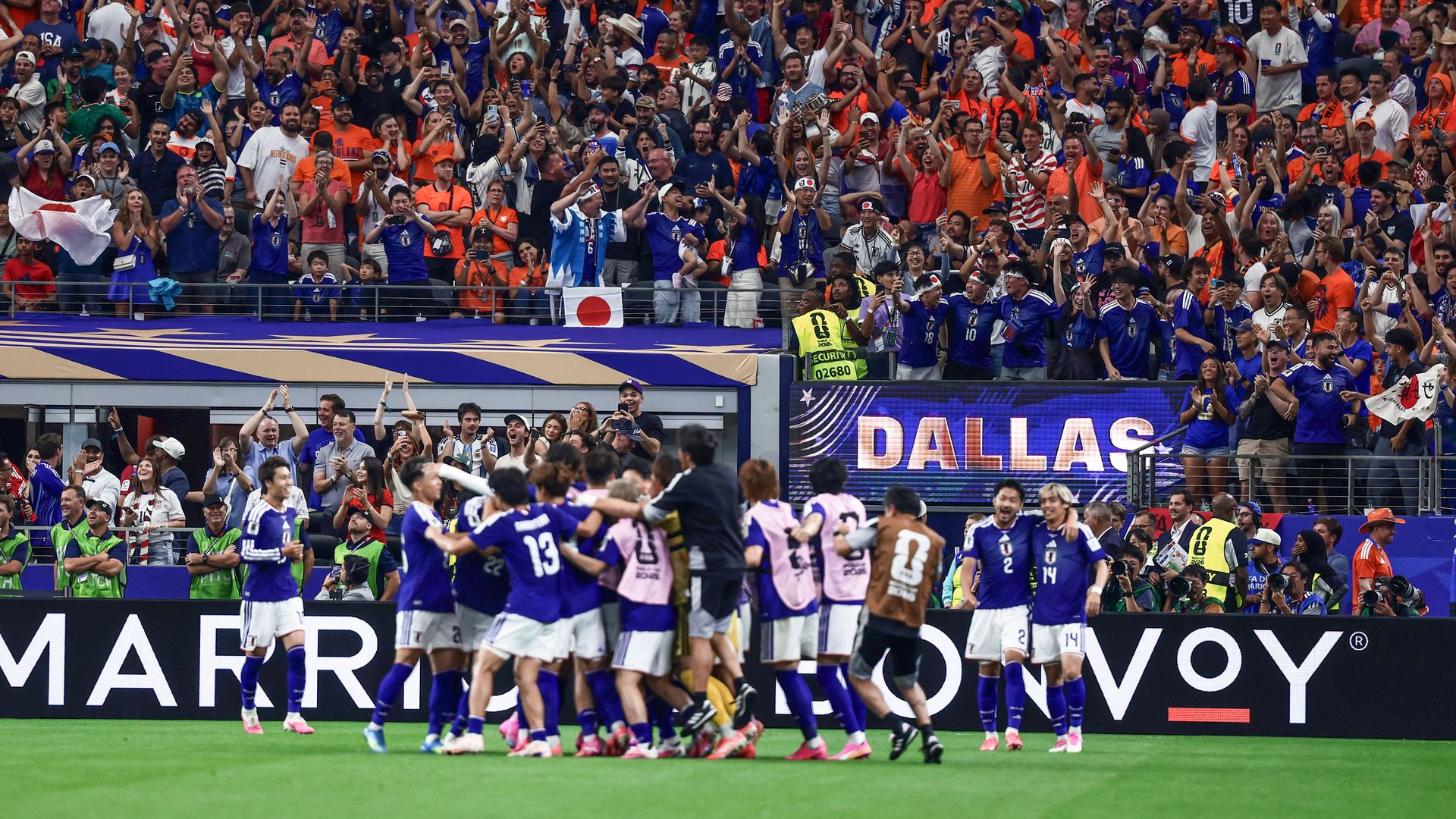 The Japan team celebrates on the field with fans behind them in the stands, cheering
