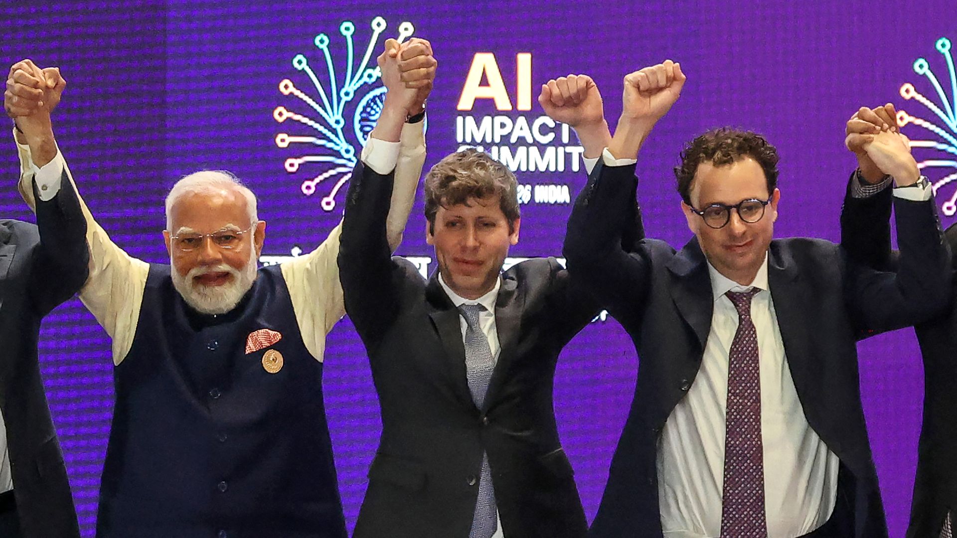 OpenAI CEO Sam Altman and Anthropic CEO Dario Amodei pose with Indian PM Narendra Modi, their arms raised in the air. 