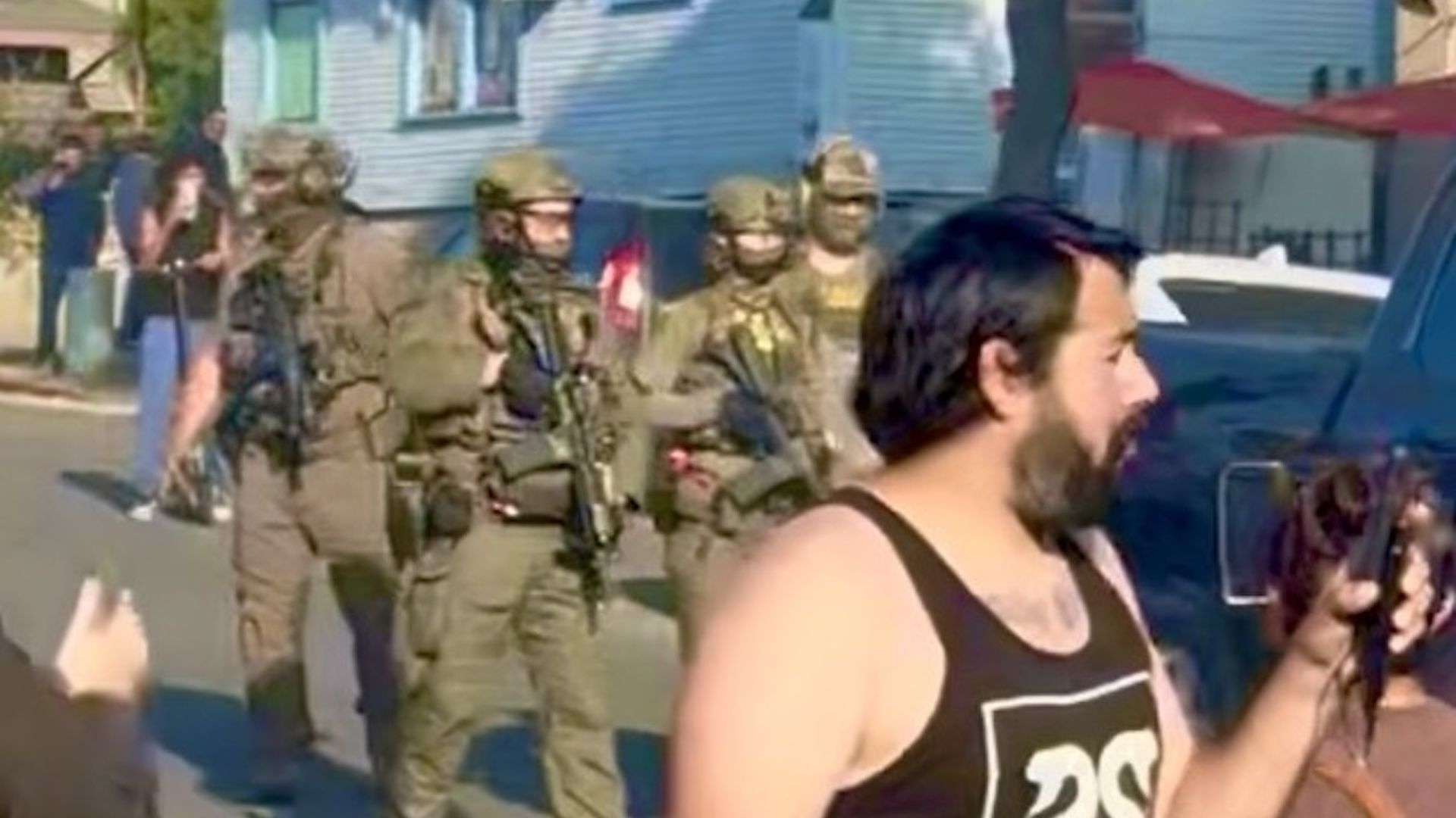 Armed ICE agents surrounded by a crowd of residents protesting the enforcement action