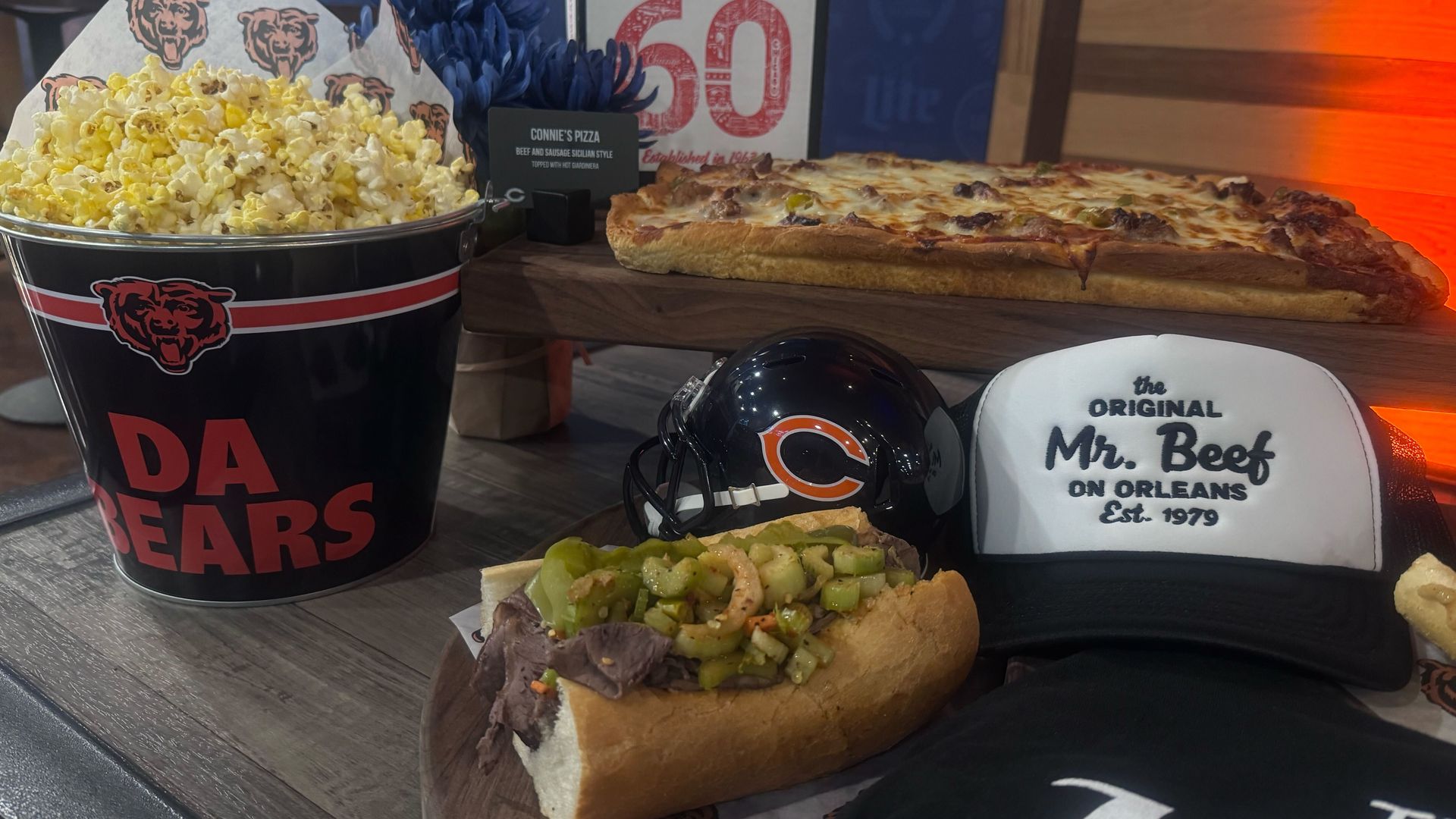 Bucket of popcorn with Chicago Bears logo, Italian beef sandwich, rectangular pizza, mini football helmet with Bears logo, and a cap reading "the ORIGINAL Mr. Beef ON ORLEANS Est. 1979".