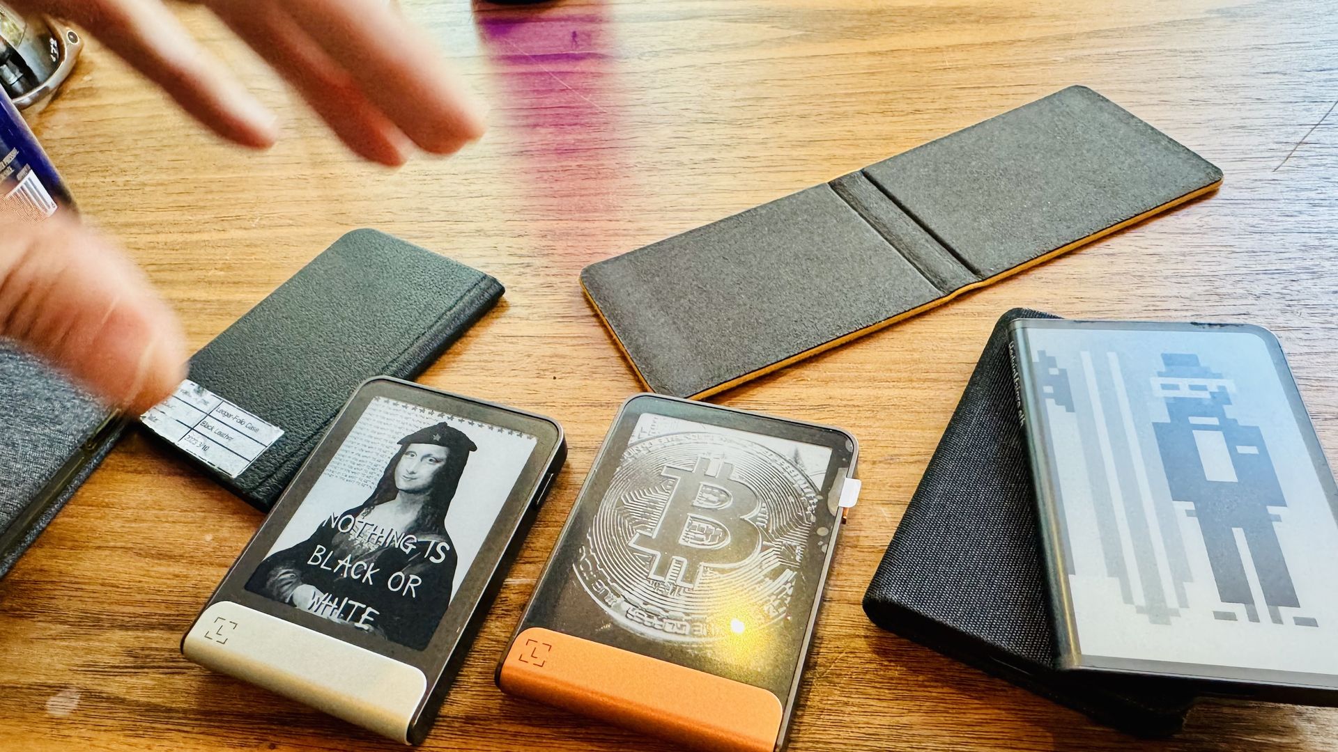 A hand reaches for Ledger crypto wallets sitting on a table. 