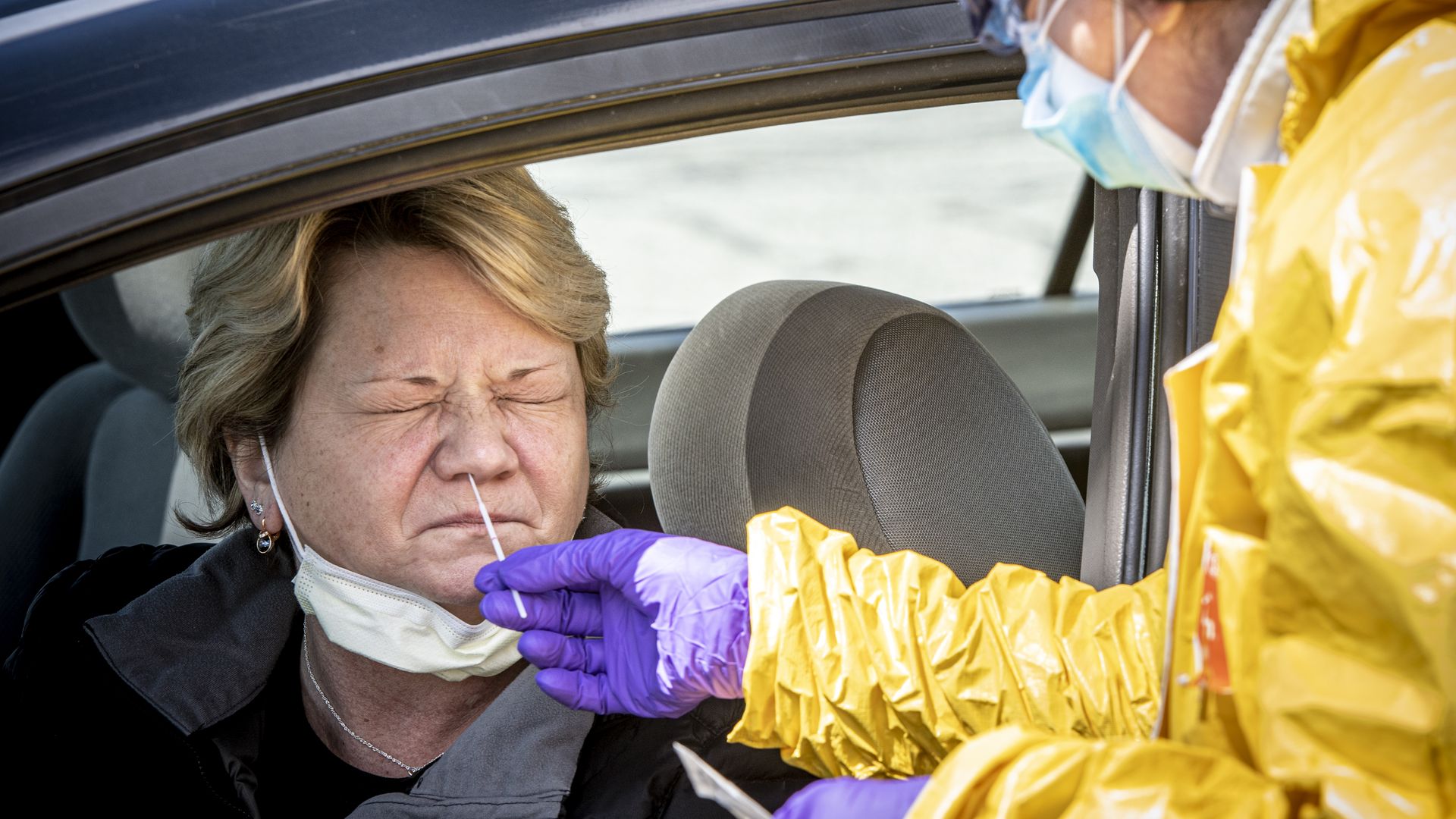 A health care worker tests a woman waiting in a car. 