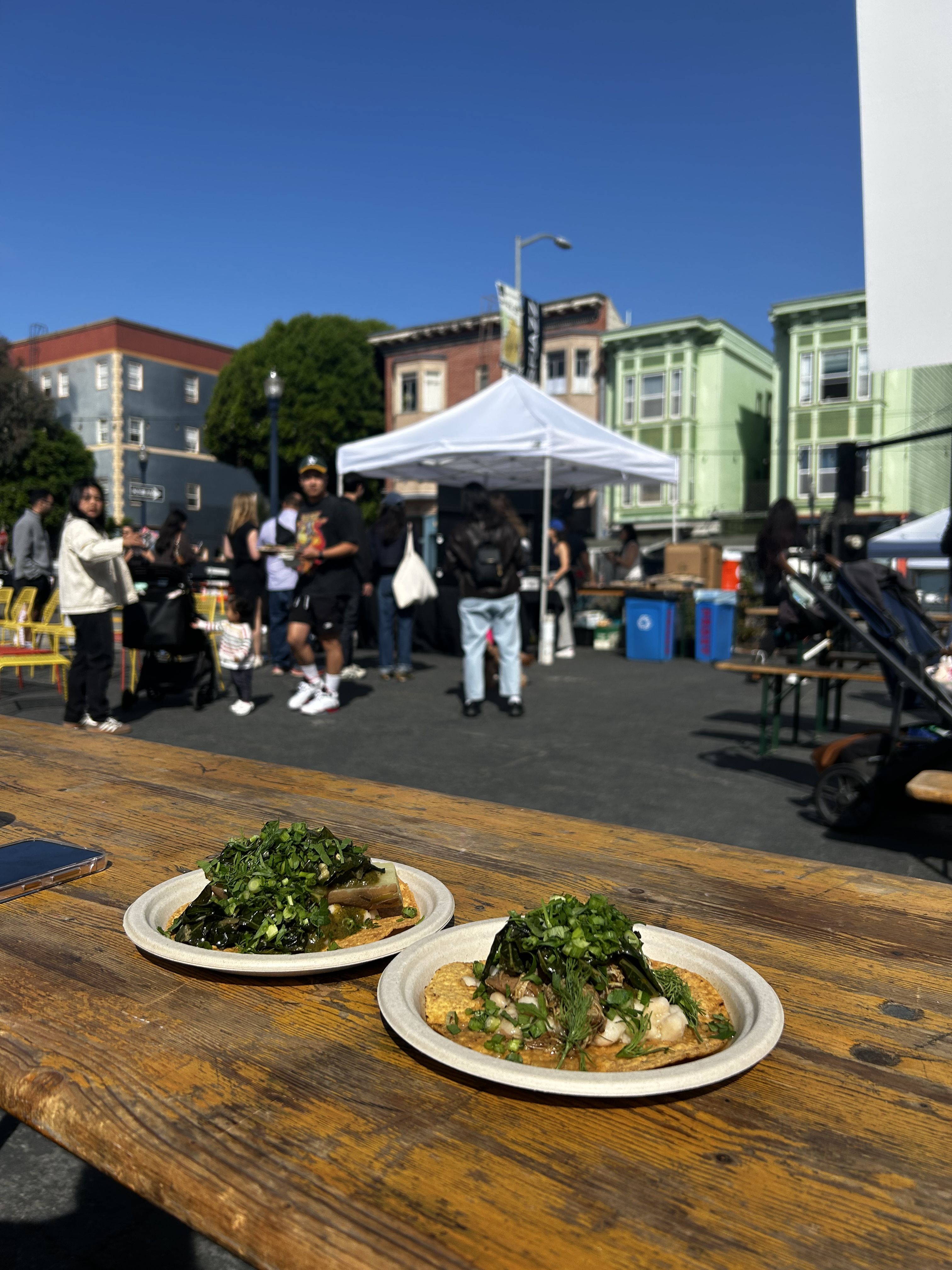 Photo of two plates of tostadas with collards and beans with people standing in the backdrop