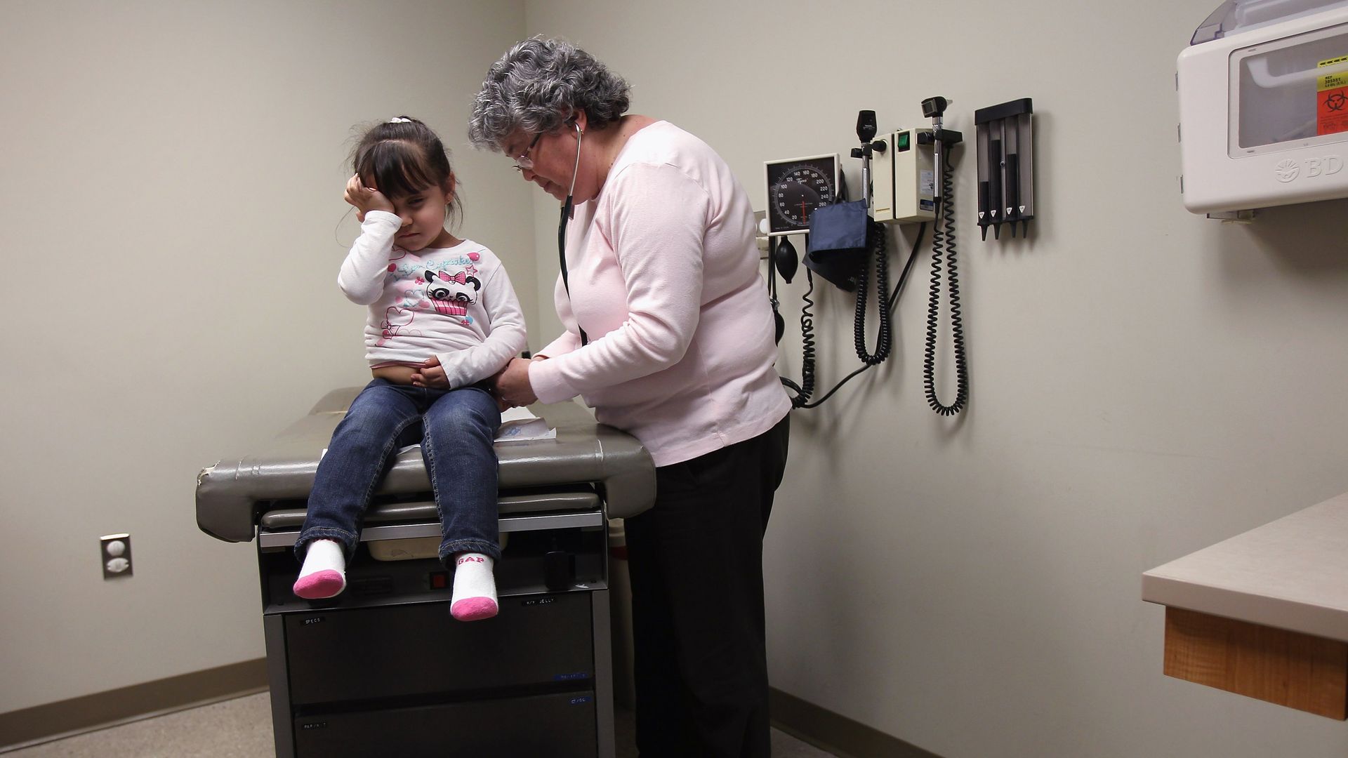 A physician assistance examines a young girl on an exam table.