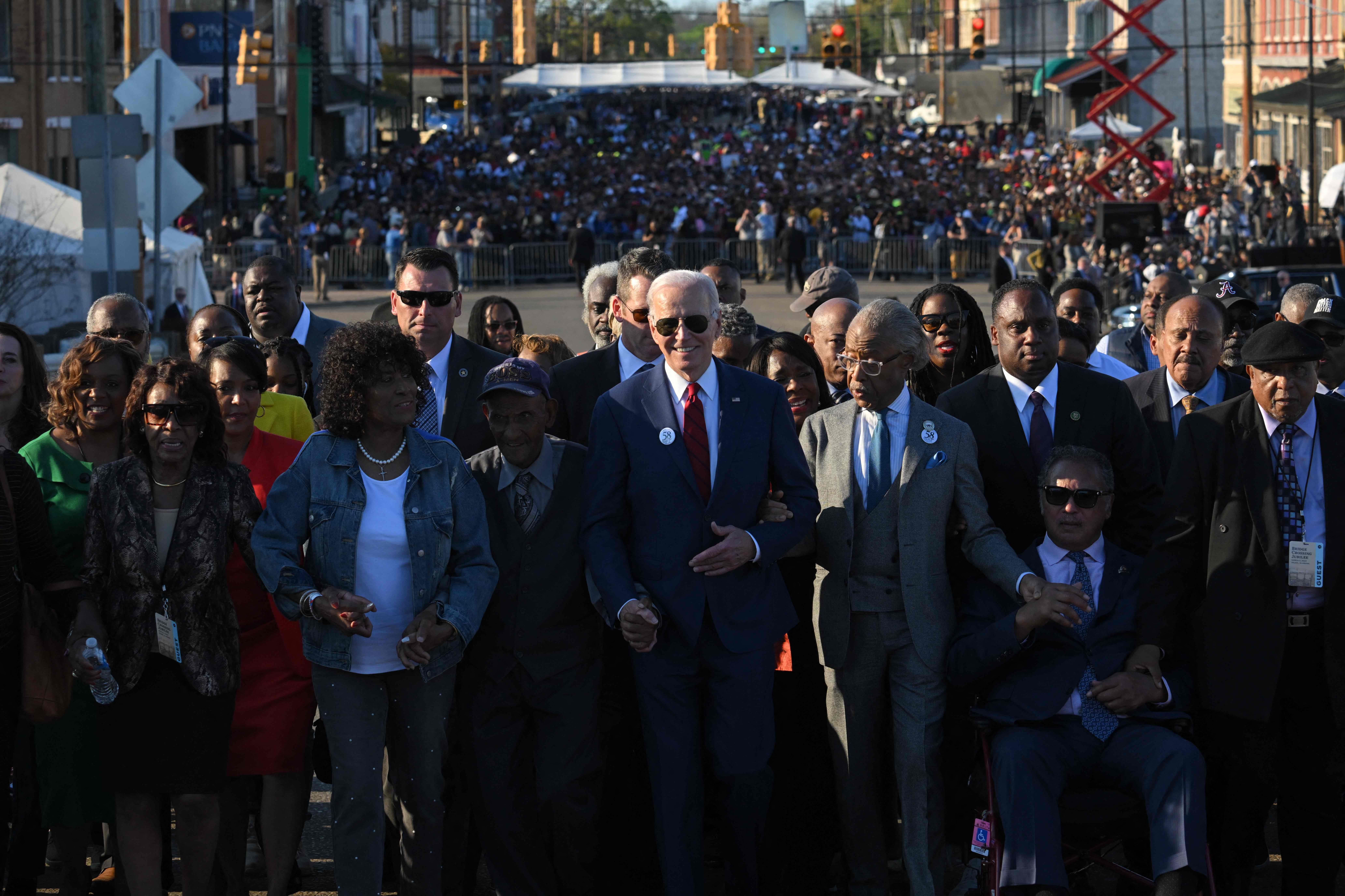 Biden surrounded by people as he crosses a bridge.