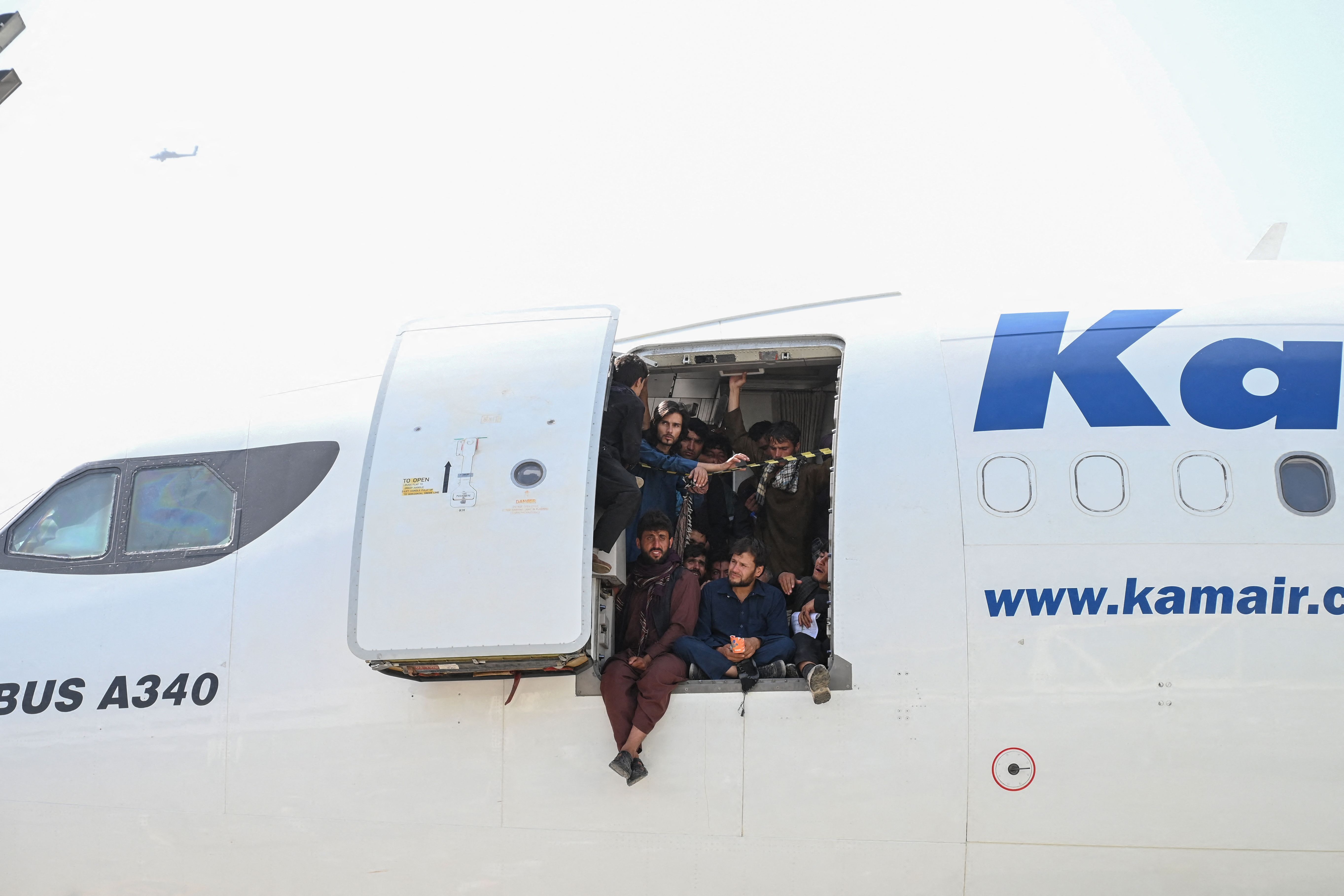 Afghan people climb up on a plane and sit by the door as they wait at the Kabul airport in Kabul on August 16