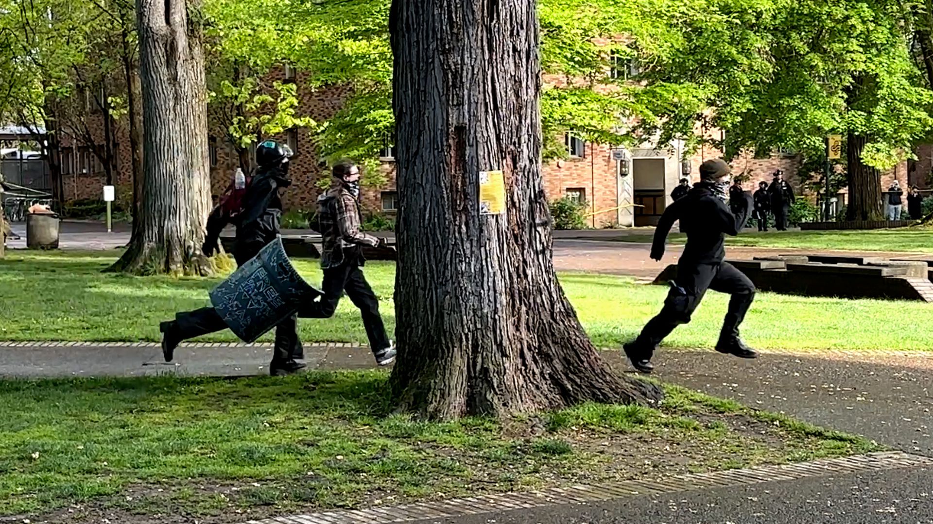 Three protestors run across a grass past a tree on Portland State Campus