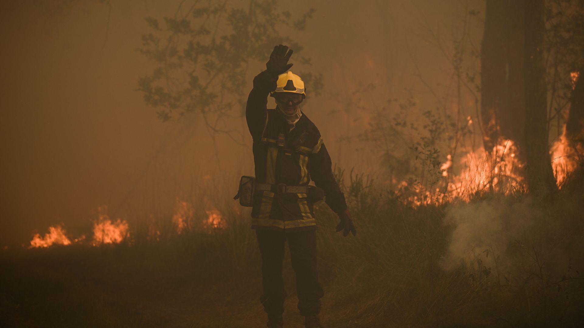 A firefighter waves to colleagues during an operation to try to control a forest fire near Louchats, some 35kms from Landiras in Gironde, southwestern France on July 18, 2022.
