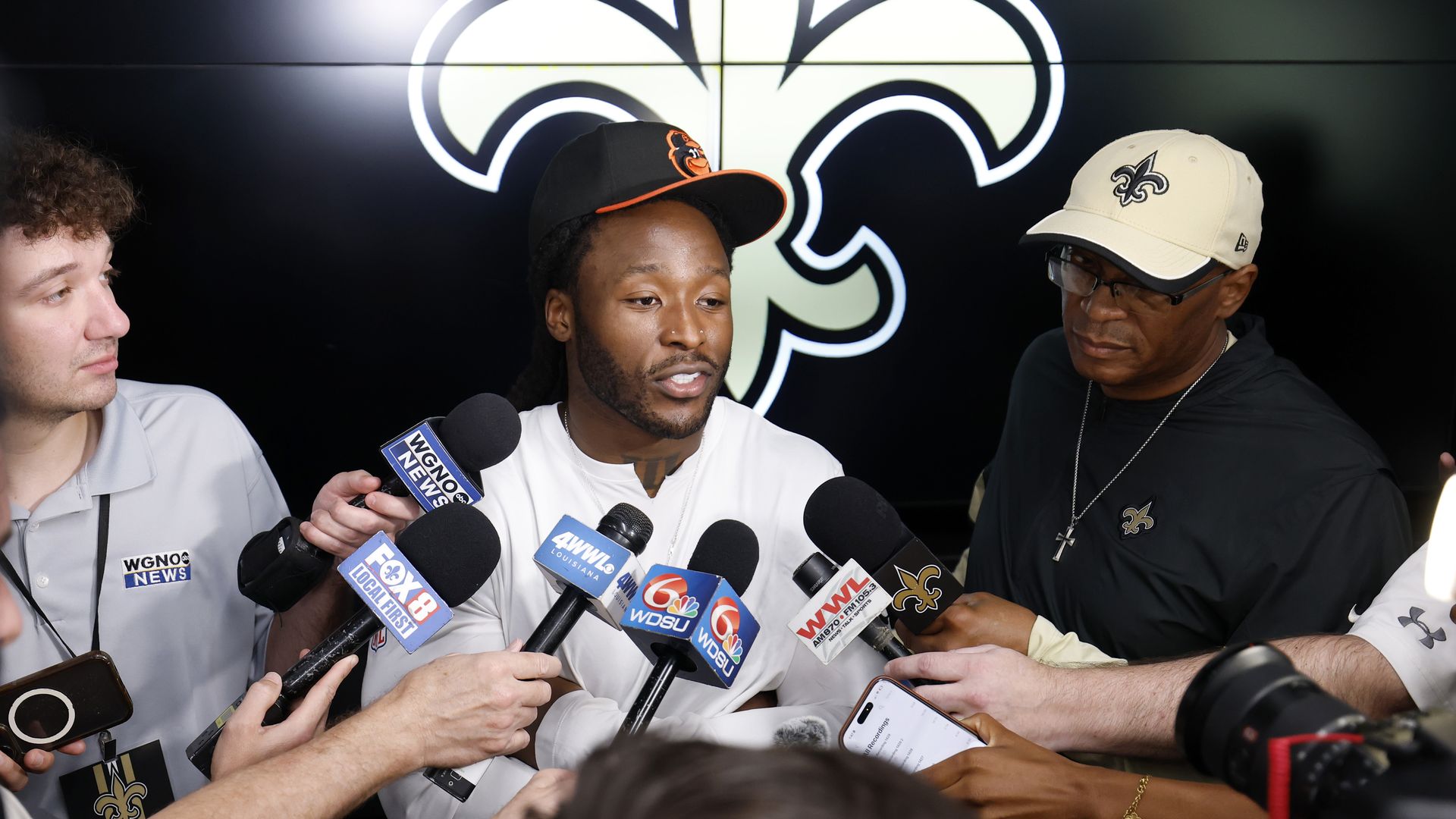Image shows Alvin Kamara talking to reporters. He's surrounded by media microphones.