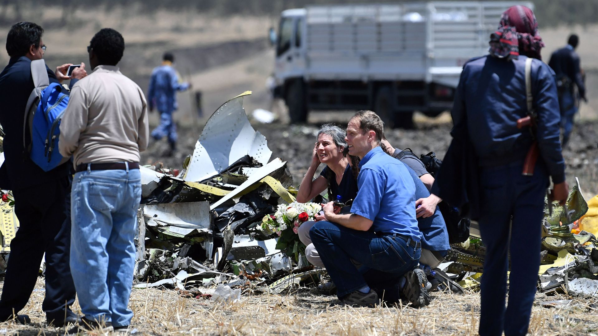 Relatives of the victims of the Ethiopian plane crash sit in a field among debris, looking concerned. 