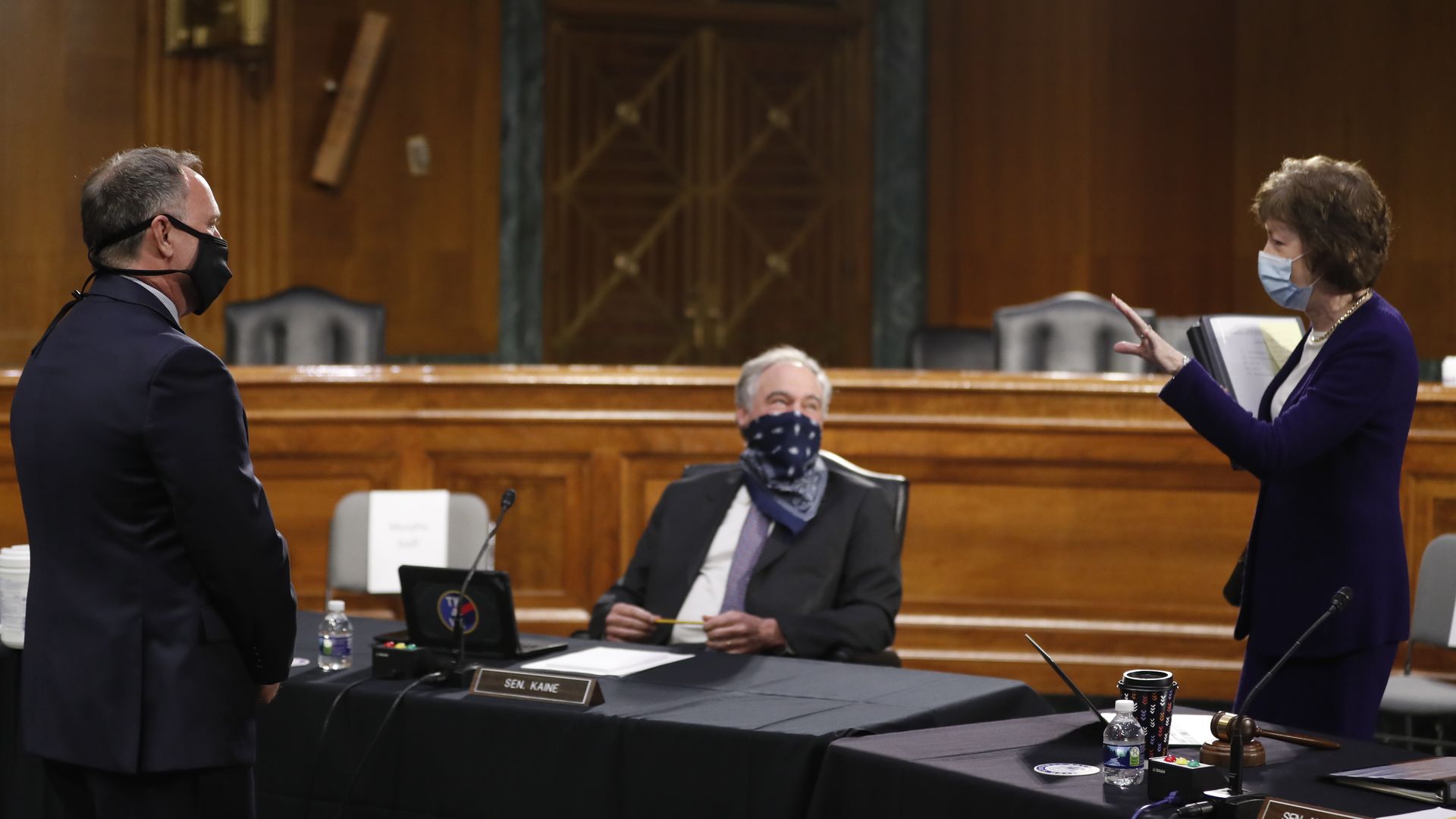 Photo of a masked Tim Kaine, Susan Collins and Gary Disbrow speaking to each other at a committee hearing