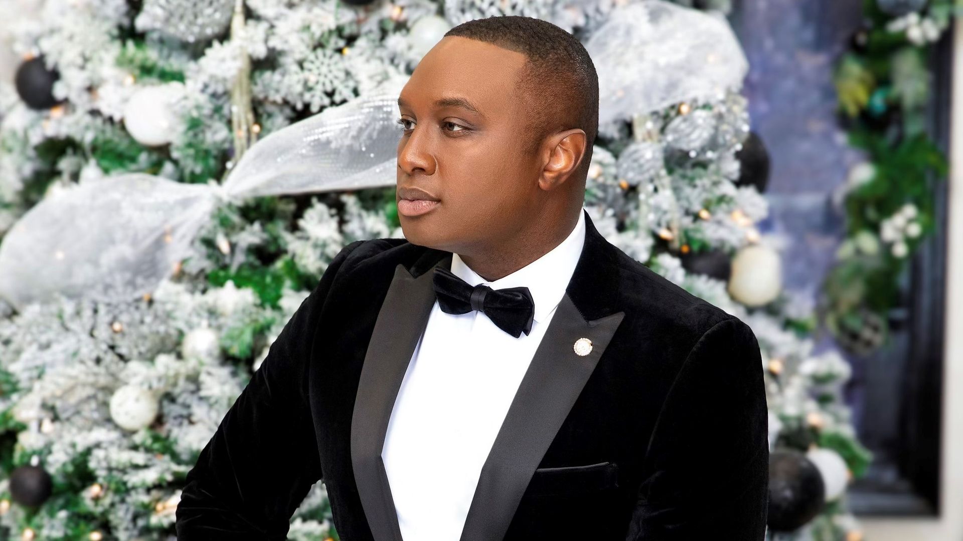 Photo of a man in a tuxedo posing in front of a decorated tree 