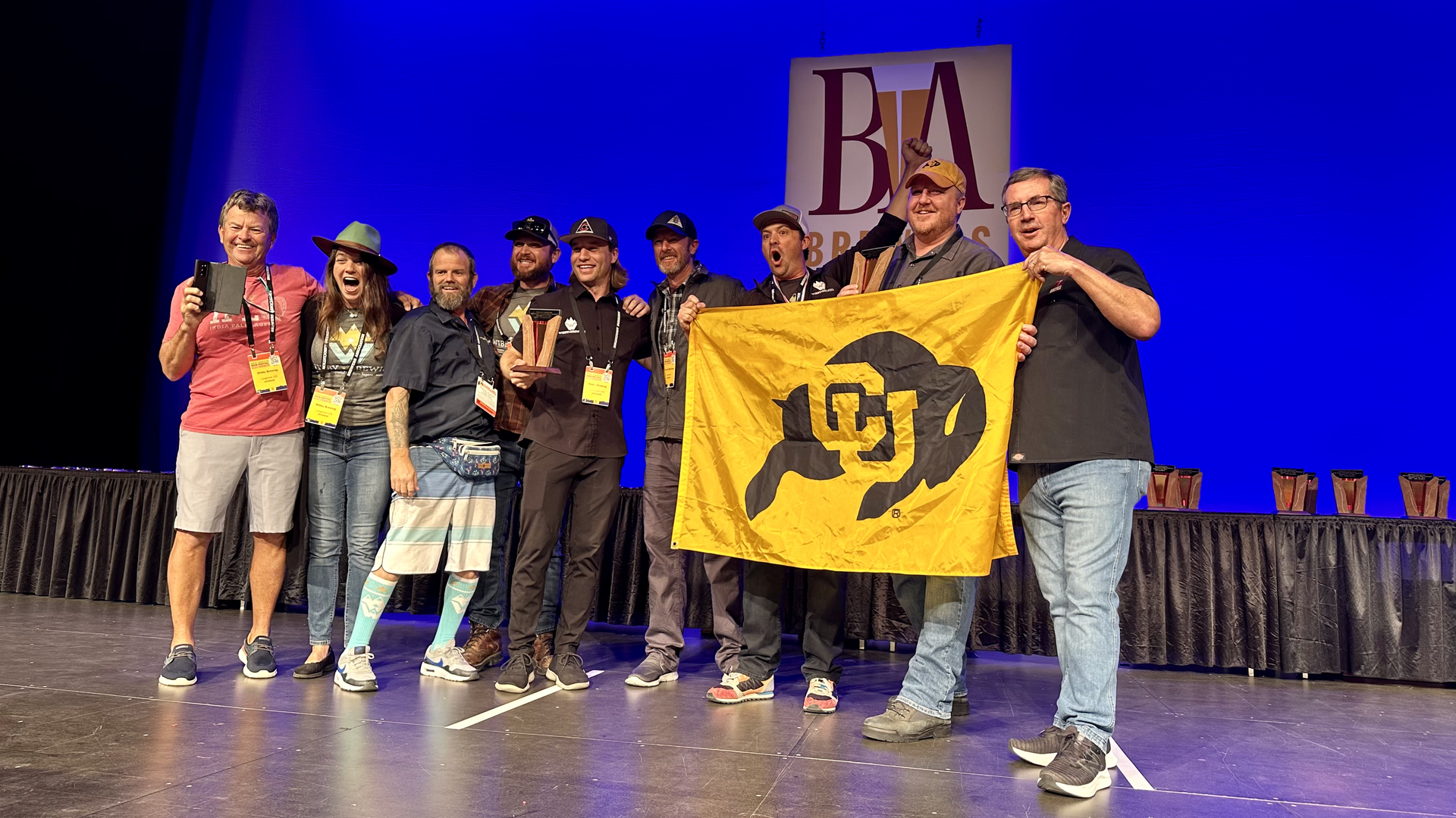 Wibby Brewing staff hold a University of Colorado flag as they accept their Great American Beer Festival trophy on Saturday in Denver. Photo: John Frank/Axios