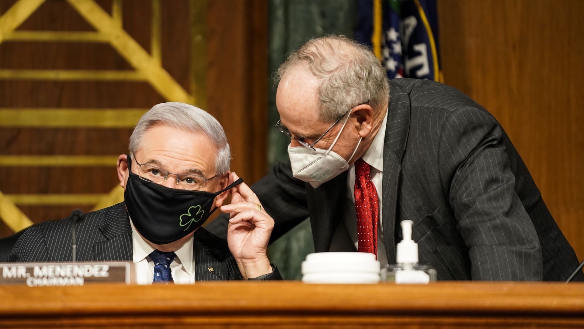Two older white men wear face masks and speak to each other while wearing suits