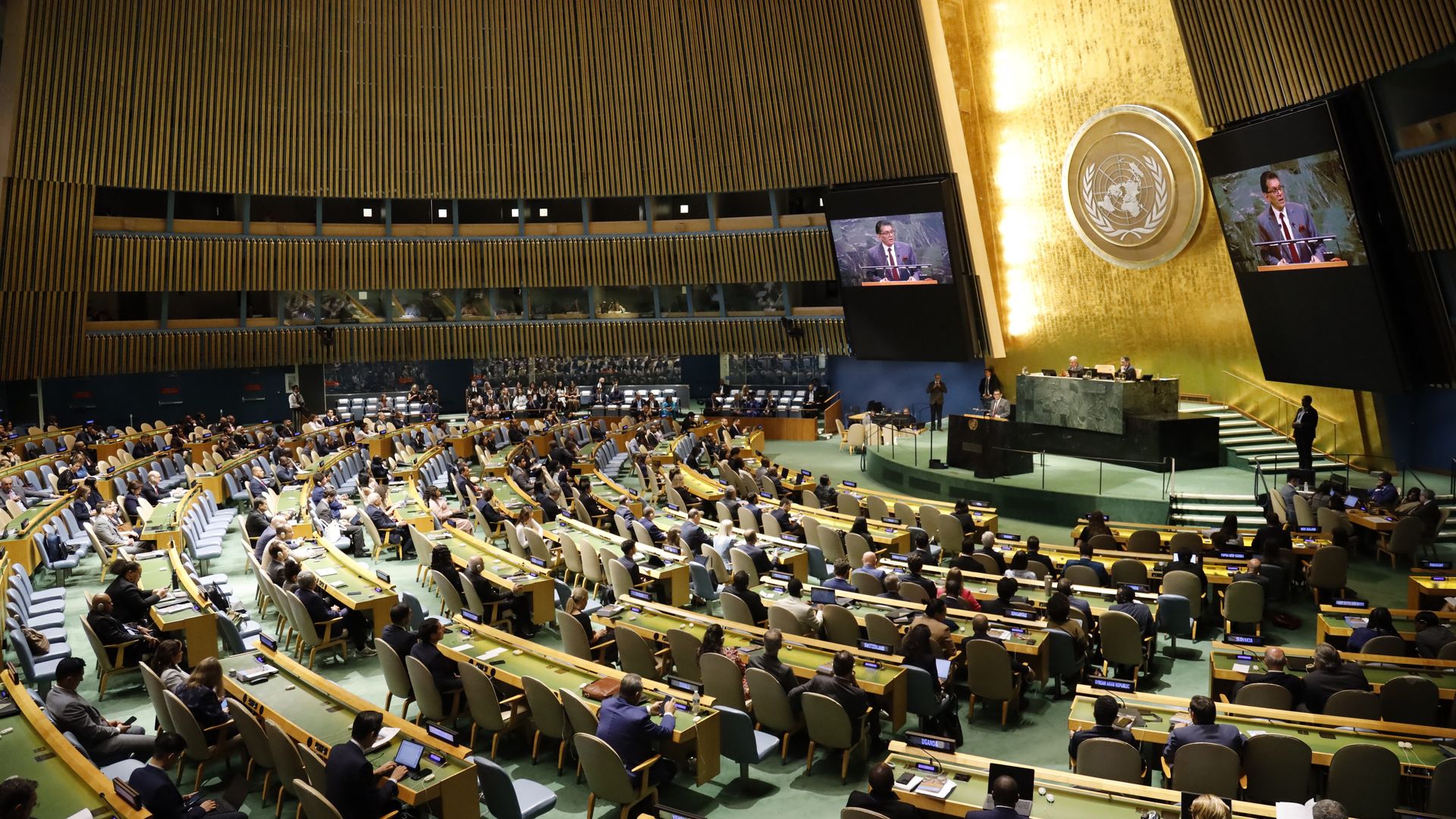 Delegates to the UN General Assembly sit in a large hall in curved rows of seats. 