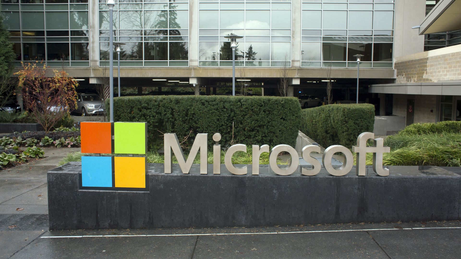 A Microsoft sign and colorful four-square logo outside the company's Redmond, Washington, campus, with trees and shrubs in the background.