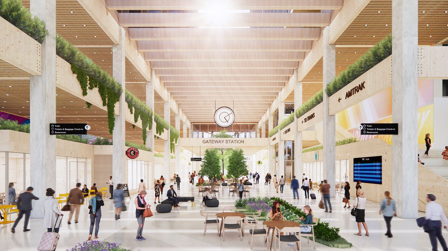 Interior of Gateway Station with high wooden ceilings, green plants hanging and potted, people walking, sitting at tables and benches, and signs for Amtrak, train, and restrooms.
