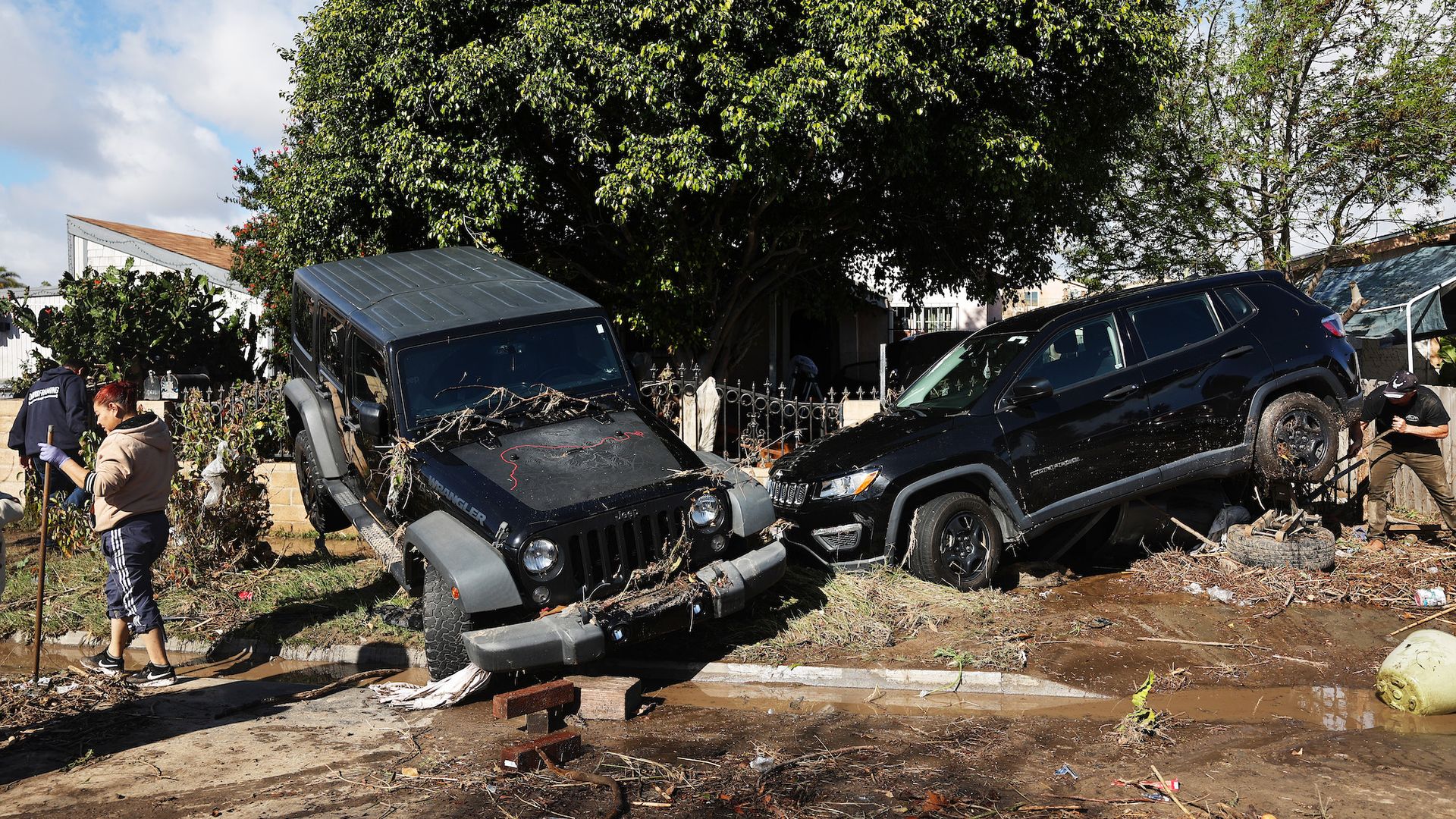A person works to help tow away two SUVs covered in debris and dislodged by flooding.