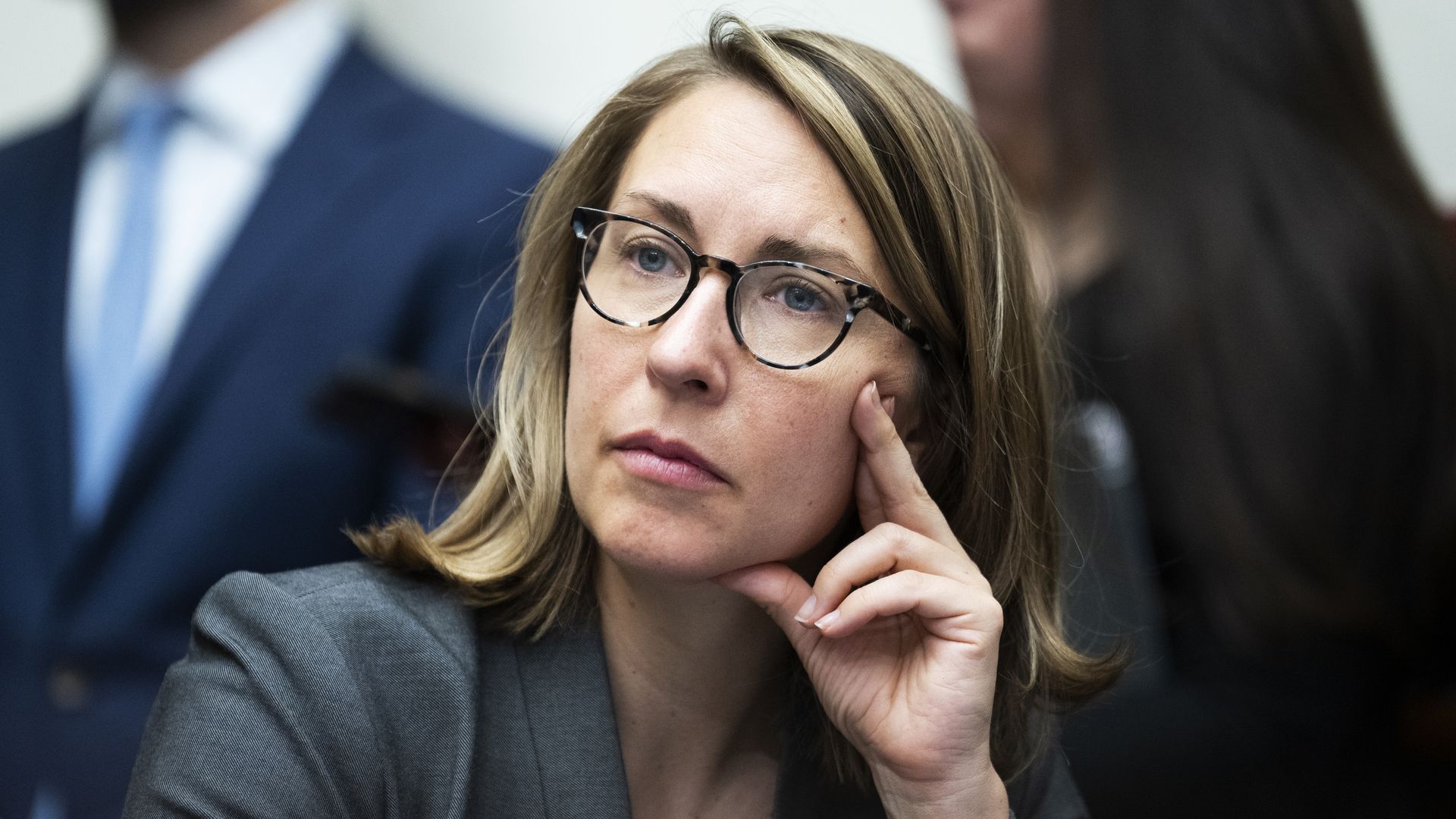 Rep. Hillary Scholten, wearing a gray jacket and glasses and putting two fingers on her cheek during a committee hearing.