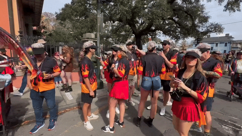 A crowd of people wearing black shirts with flames on them wave at a camera.