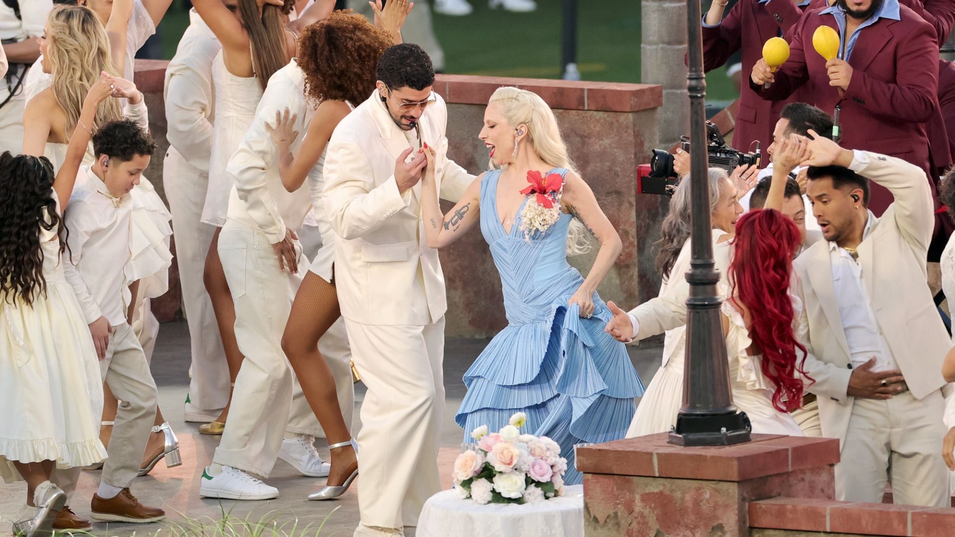 Bad Bunny in a white suit and Lady Gaga in a blue dress with a red and white corsage dancing salsa among other adult and kid dancers during the Super Bowl half time show.