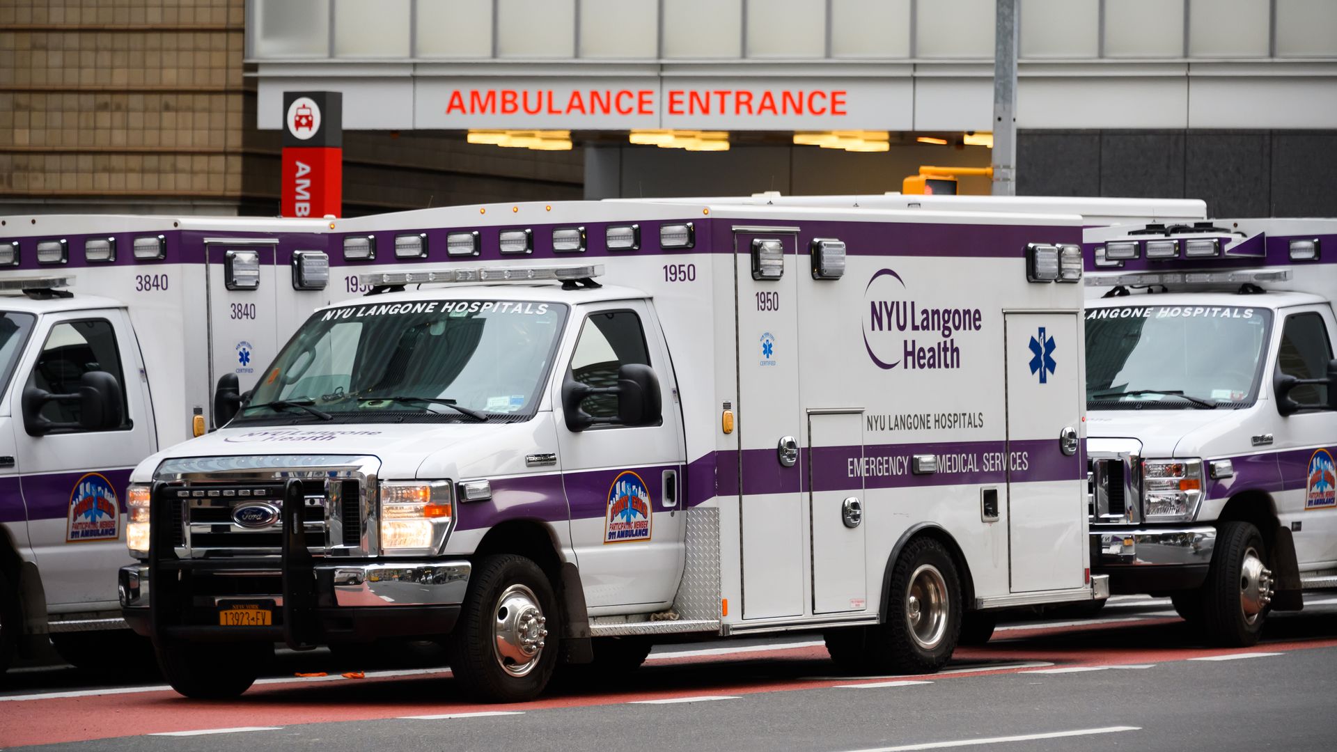 A white and purple ambulance with the NYU Langone logo and emergency room in the background.