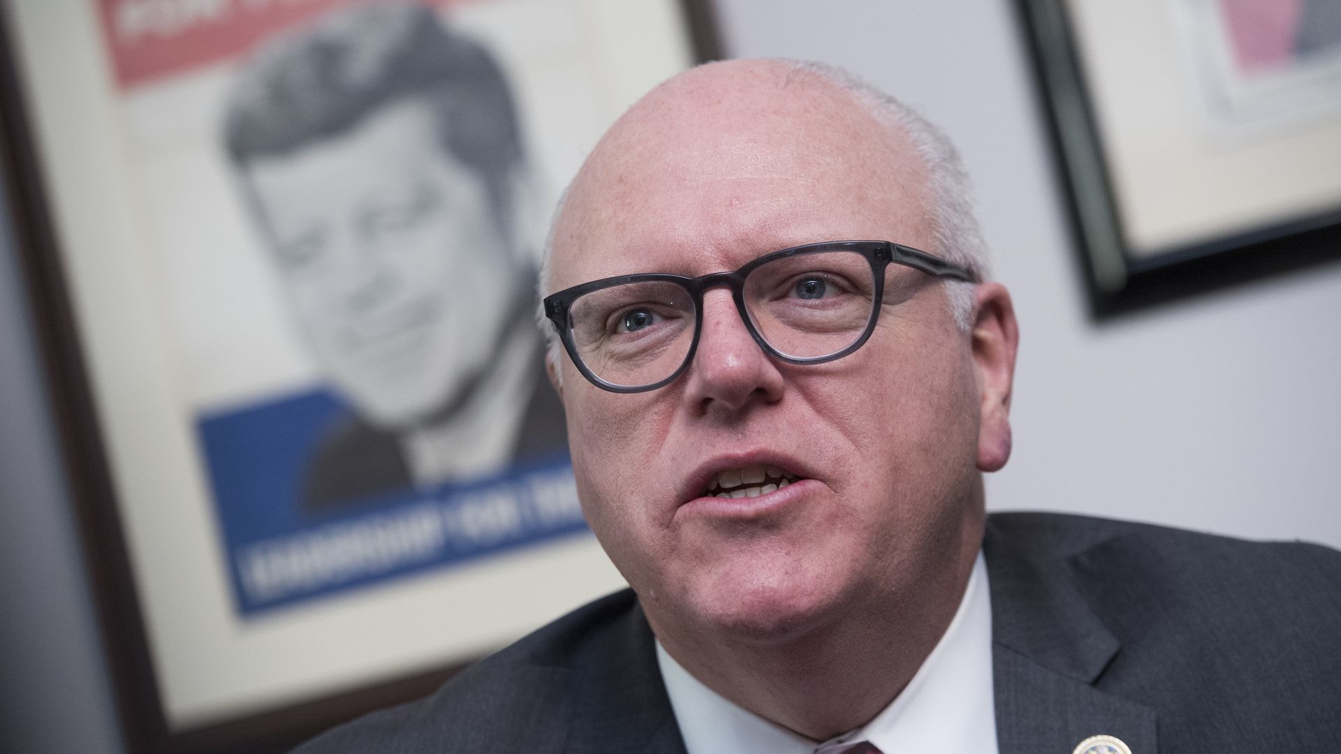 Former Rep. Joe Crowley is seen speaking in front of a 1960 "JFK For President" campaign poster.