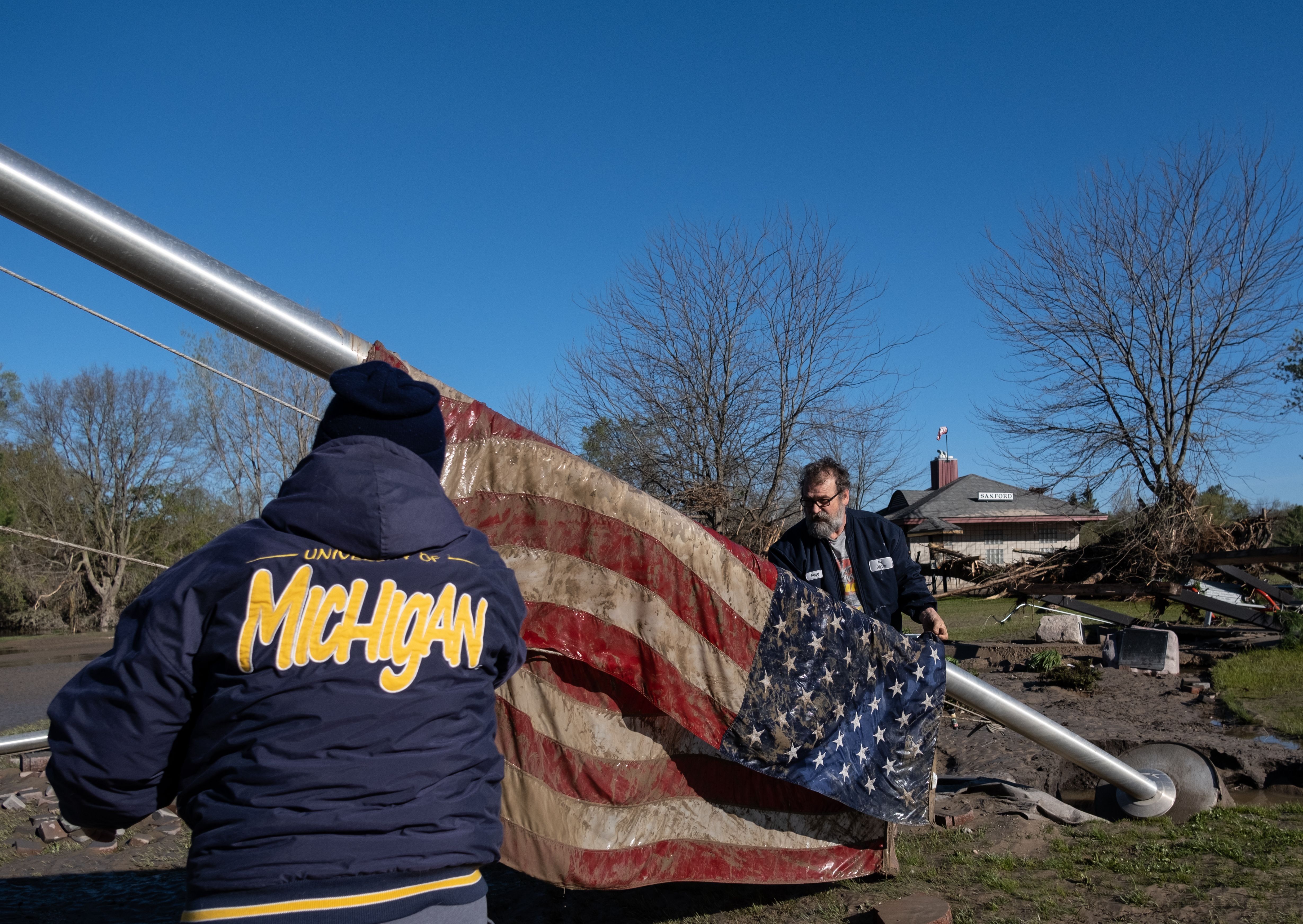 In this image, two people lift a large muddy American flag 