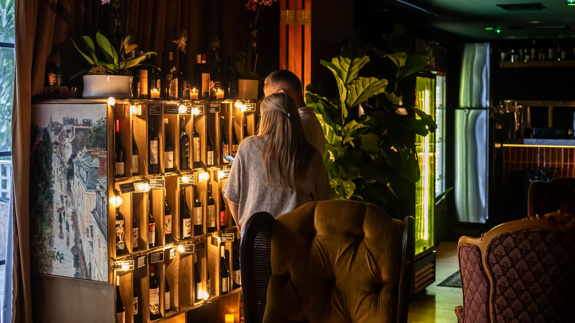 Two people standing in front of a wine cabinet. 