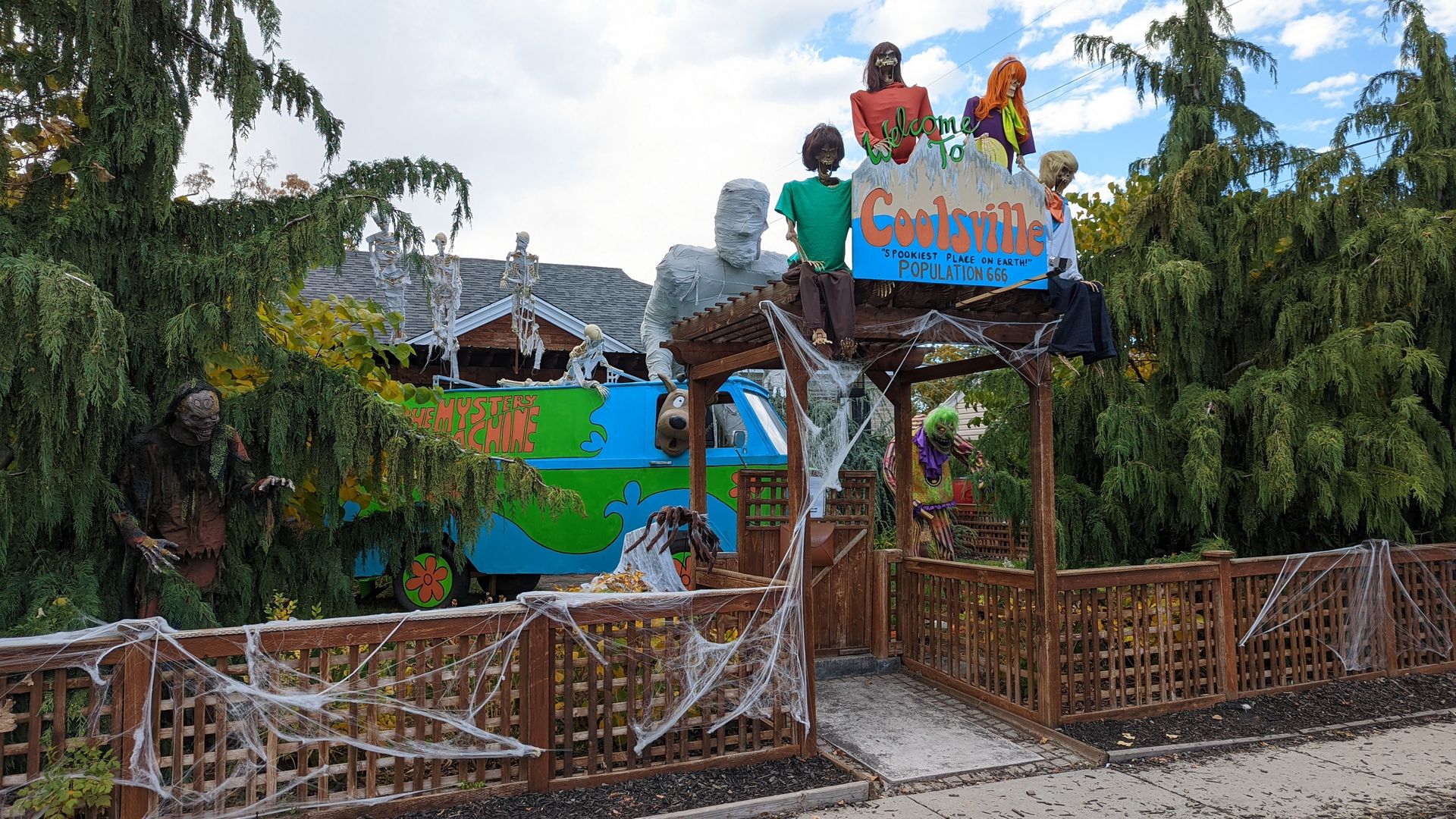 Halloween decorations depicting Scooby Doo and the gang outside a home with conifer trees.